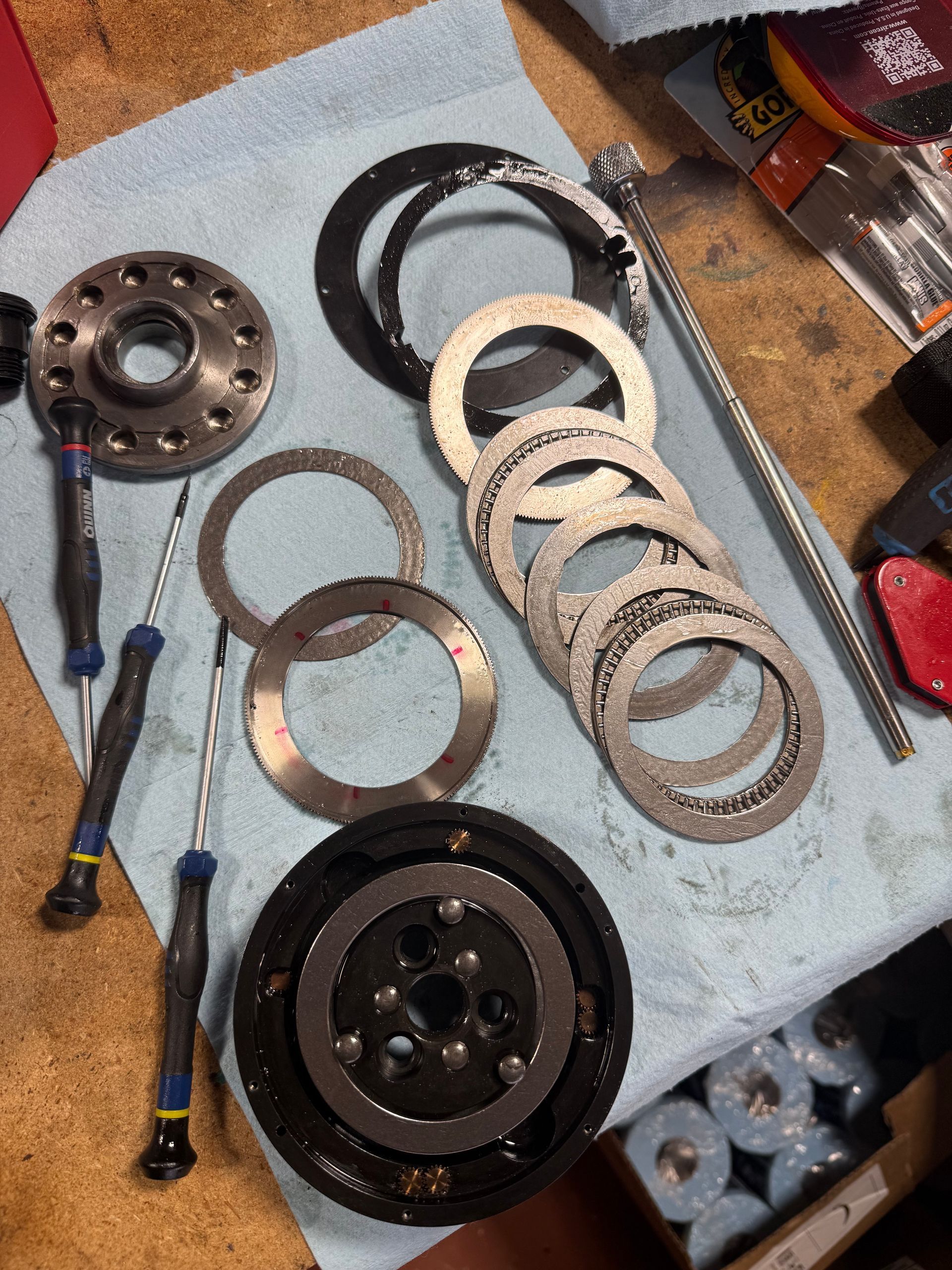 Assorted metal gears, rings, and tools laid out on a blue cloth during mechanical work.