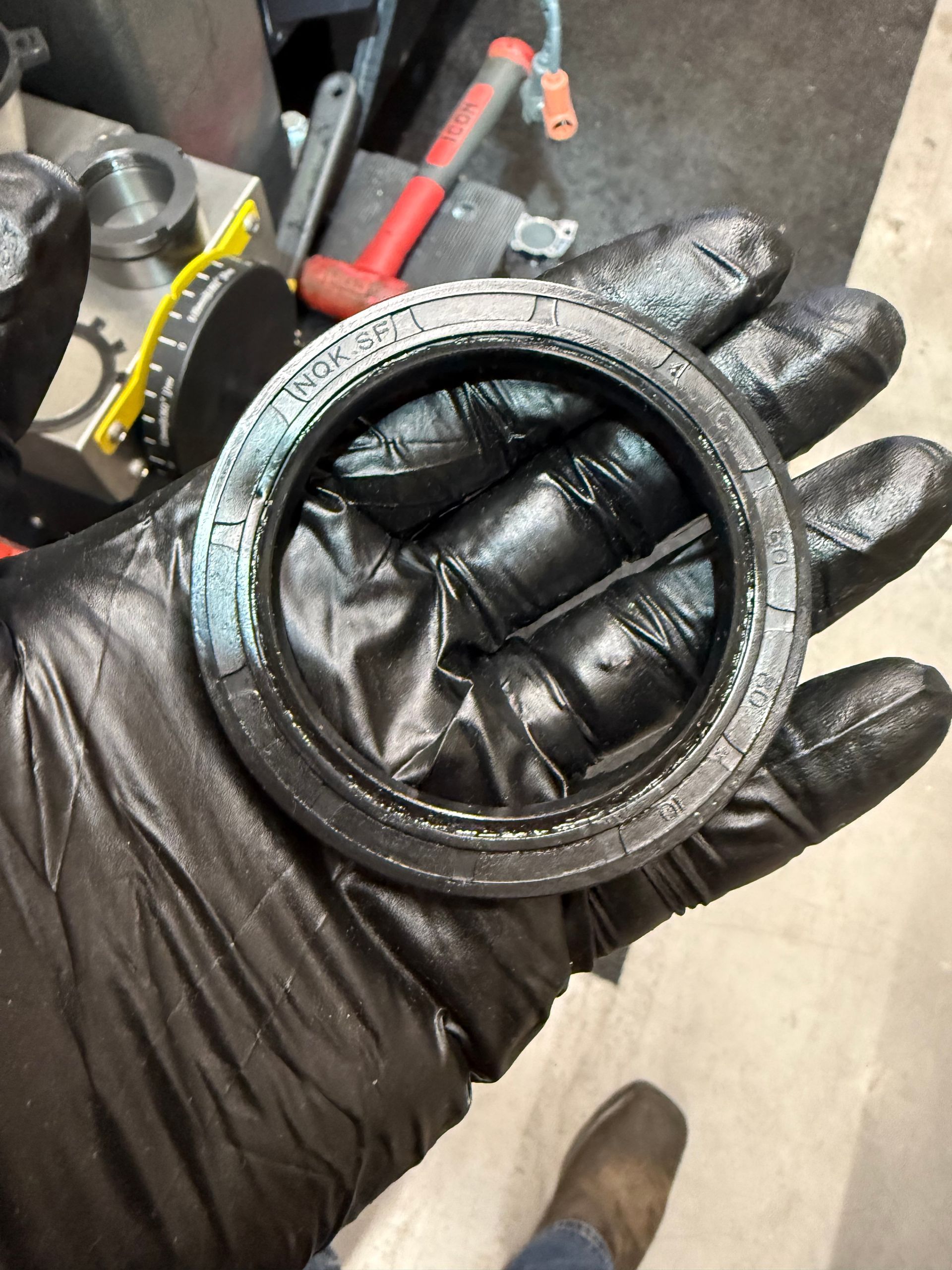 Gloved hand holding a circular black rubber seal in a workshop.