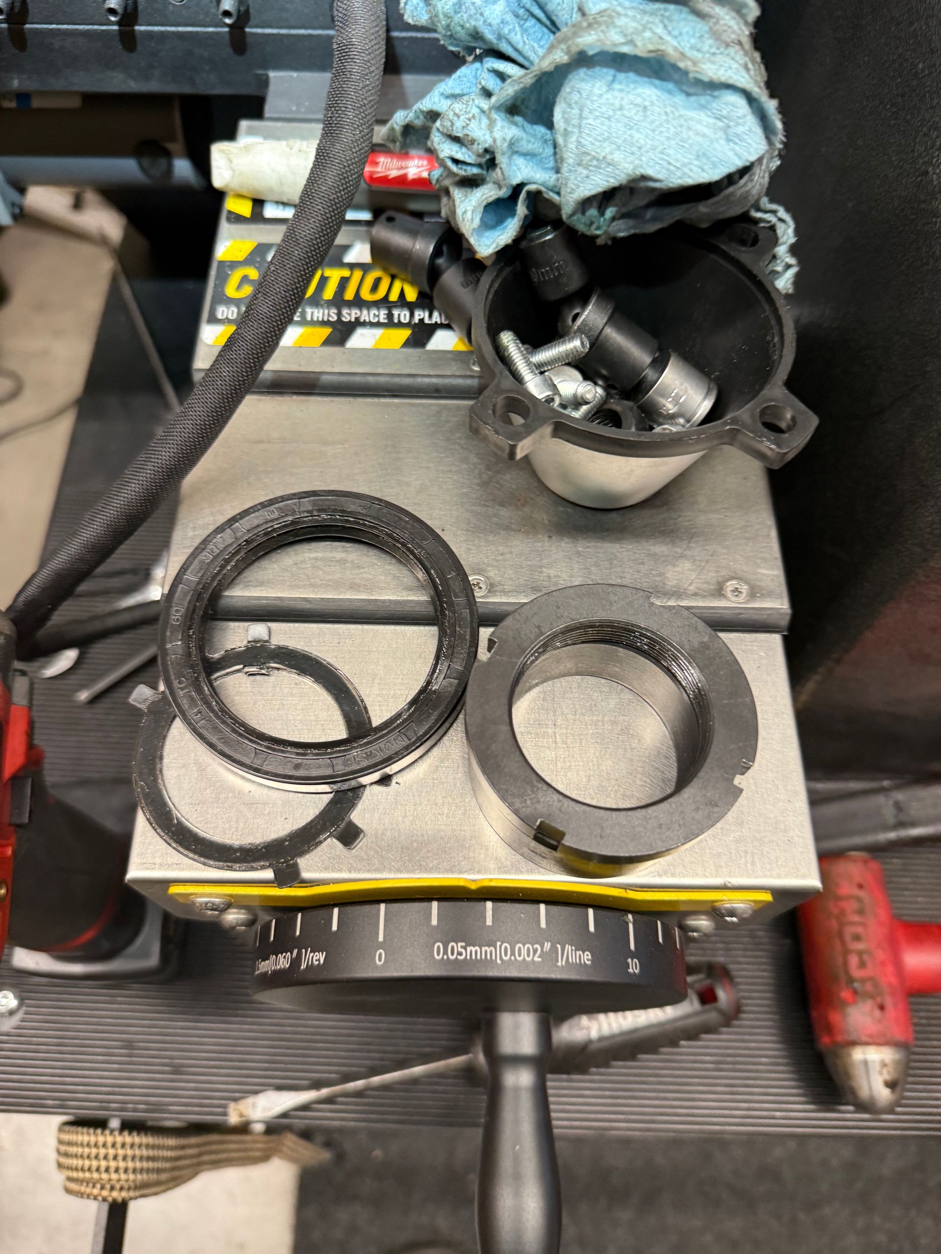 Workshop bench with metal rings, braided cable, and a gloved hand holding a black hose on a machine platform.