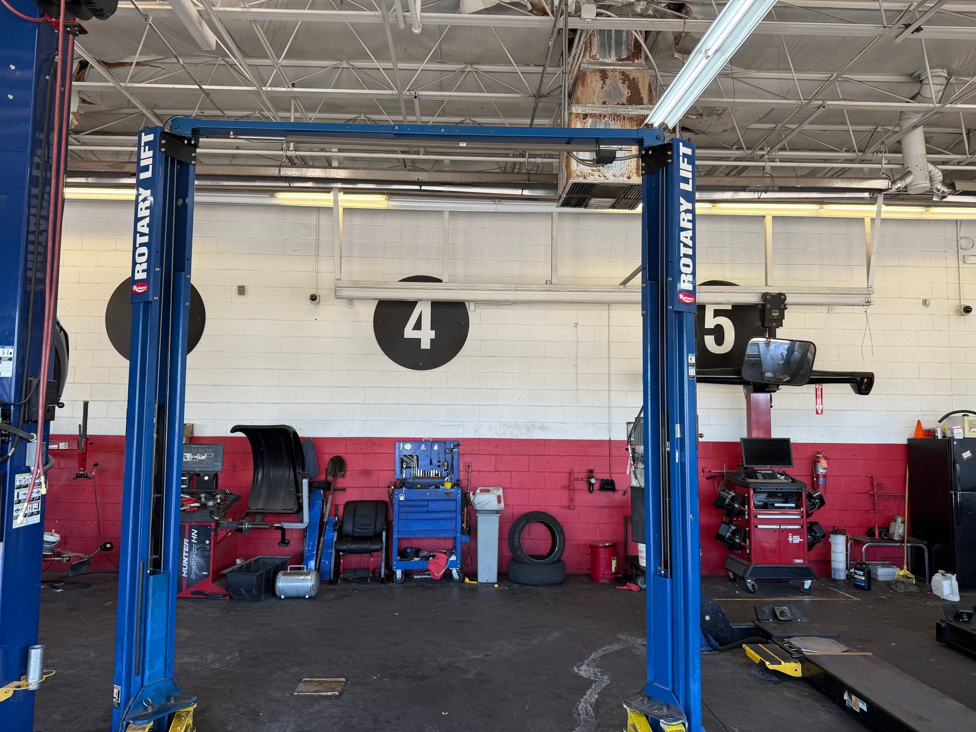 Auto repair shop interior with blue car lifts, red wall, and tools along the back wall.