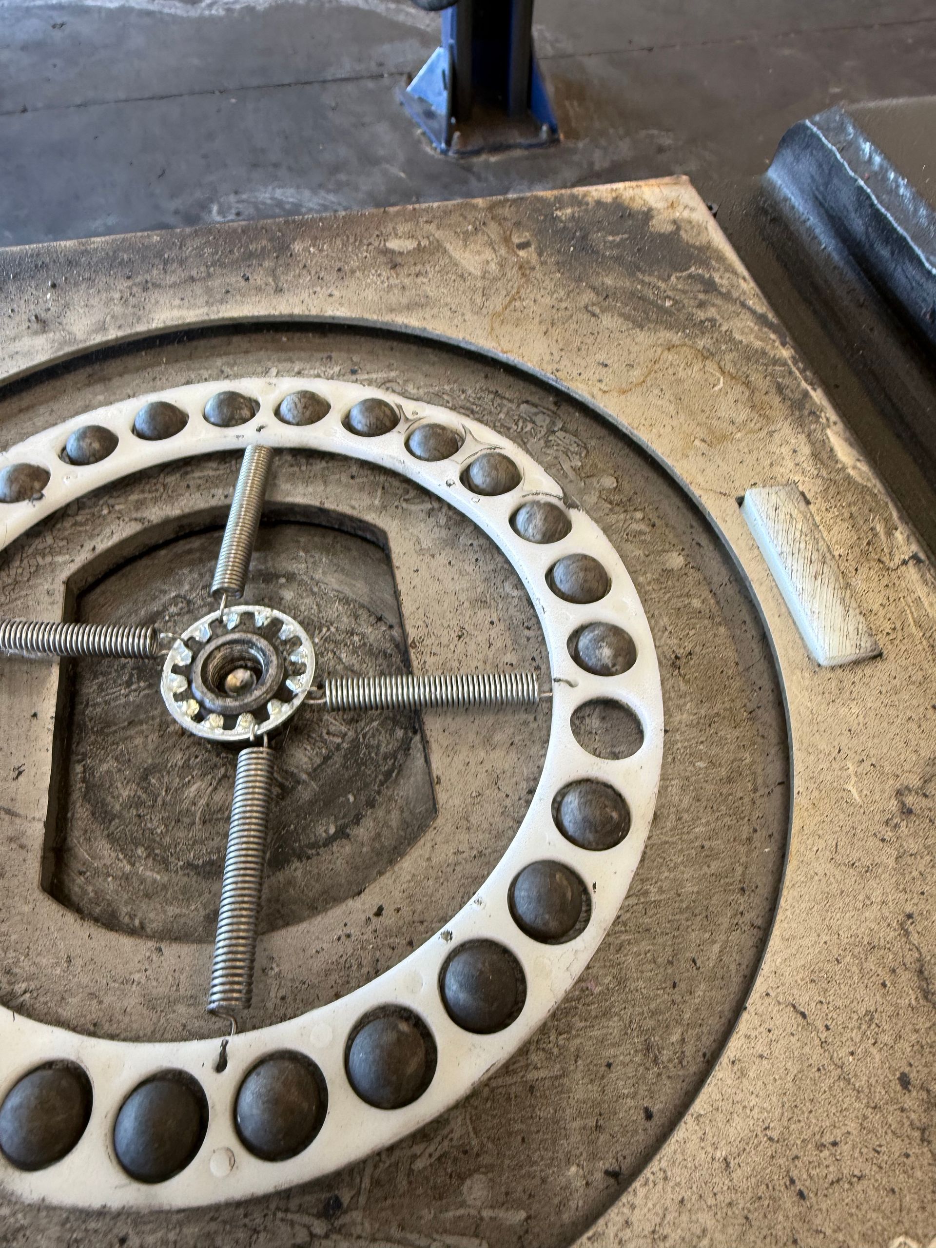 Close-up of a metal circular machine part with bolts and a central gear on a workshop floor