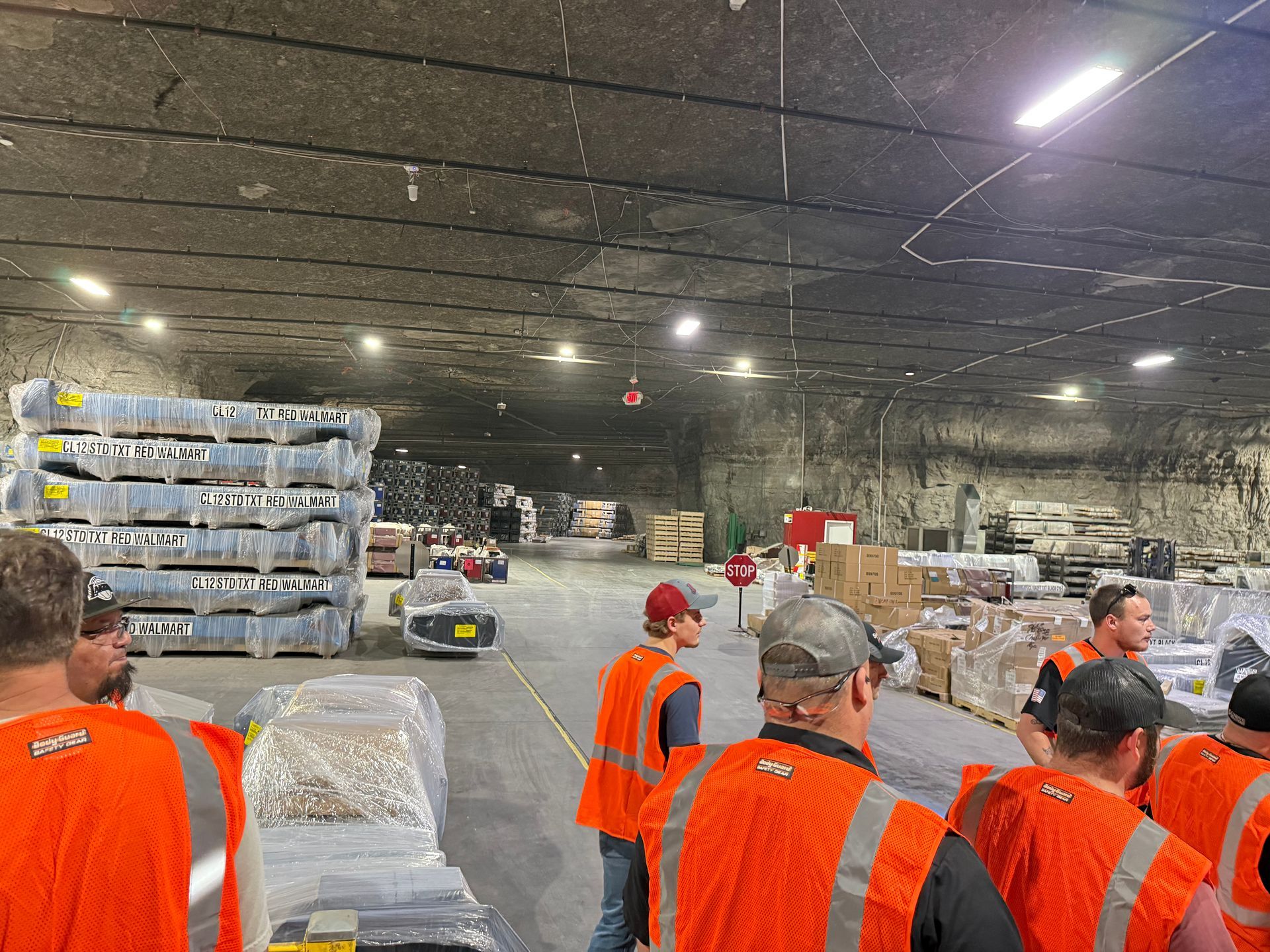 Workers in orange vests sorting pallets inside a large warehouse aisle