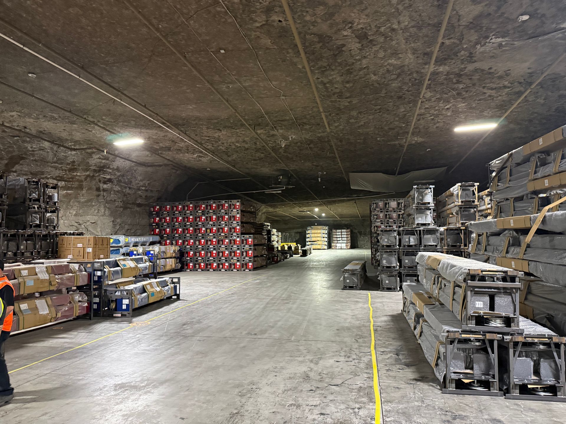 Warehouse aisle with stacked boxes and pallets under a low, dark ceiling