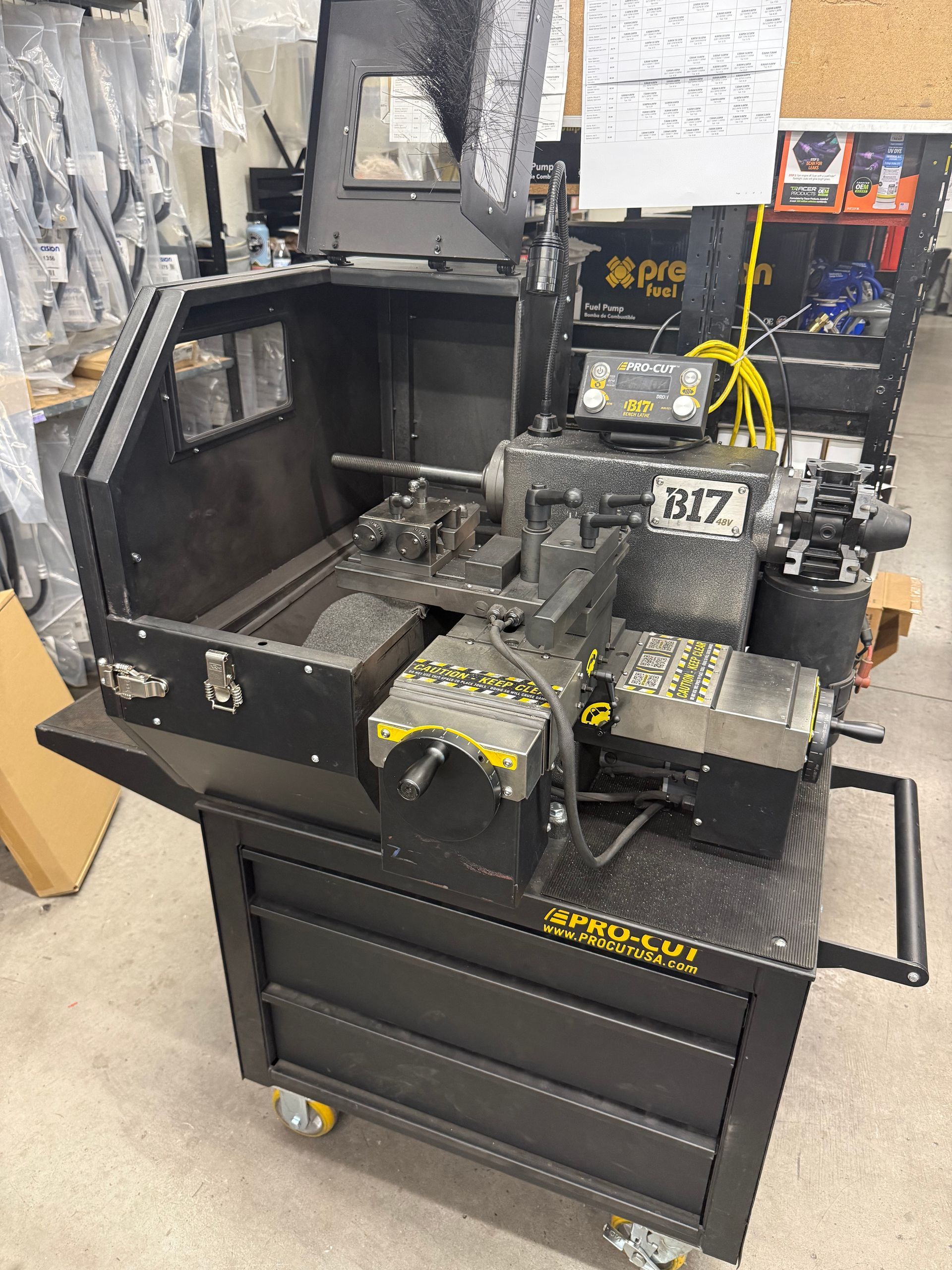 Black tool cart holding a large metal machine in a workshop, with boxes and yellow cables nearby