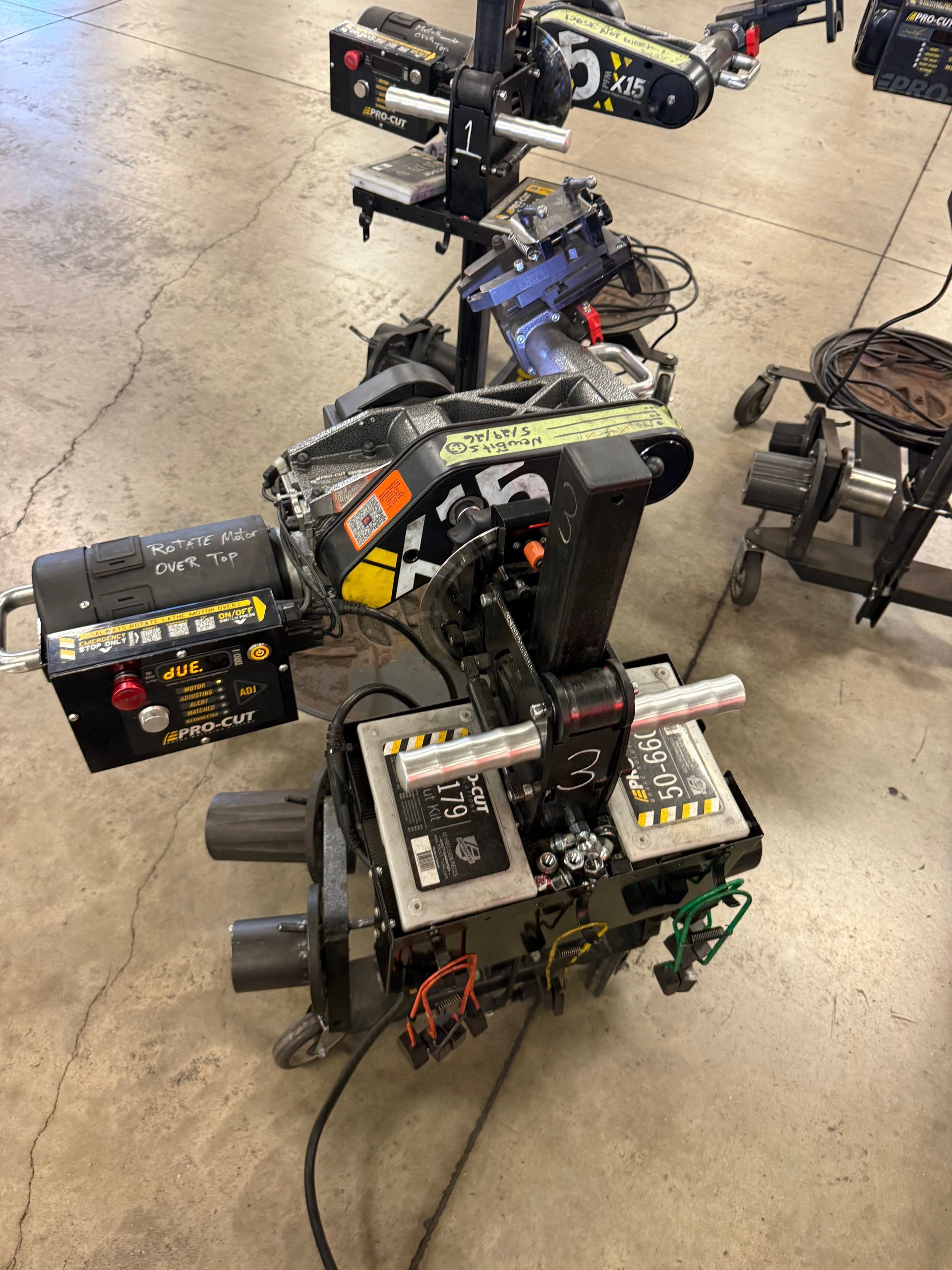 Several small wheeled robots on a concrete floor, with wires and mounted components, likely in a workshop or lab.