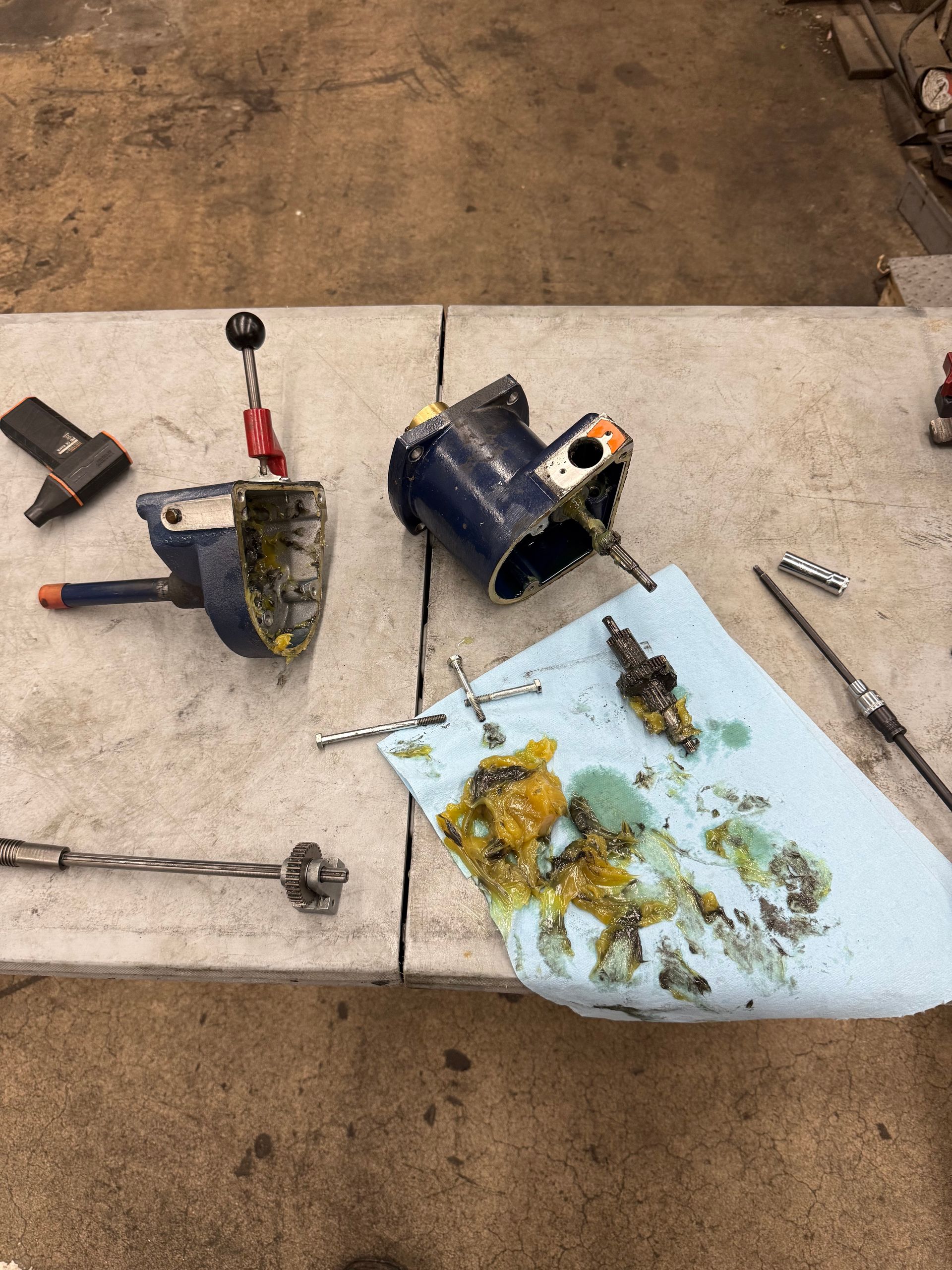 Scattered mechanical parts and tools on a concrete surface beside a blue towel with oily debris.