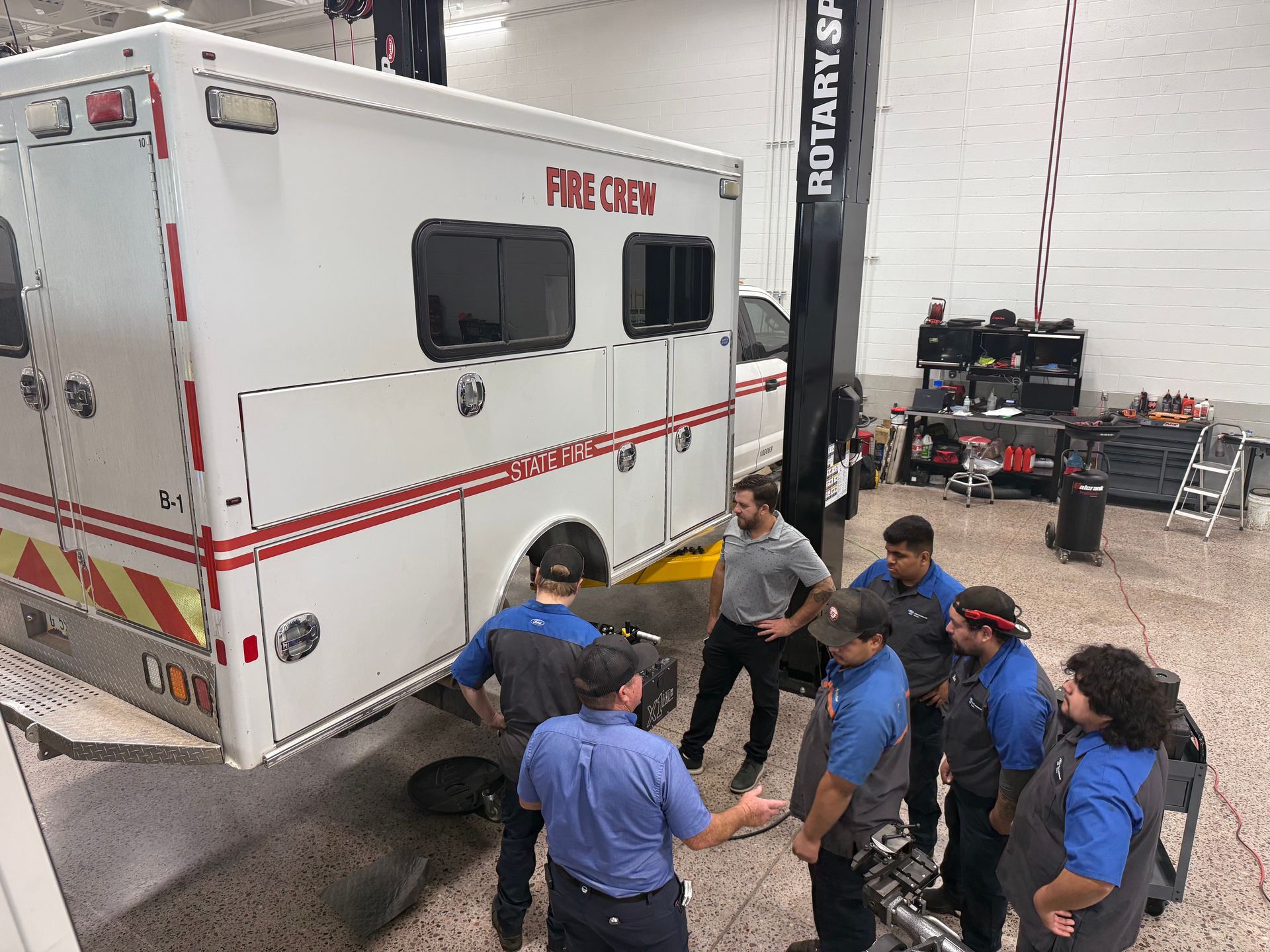 Rescue crew huddles beside a white fire truck in a garage, preparing equipment.