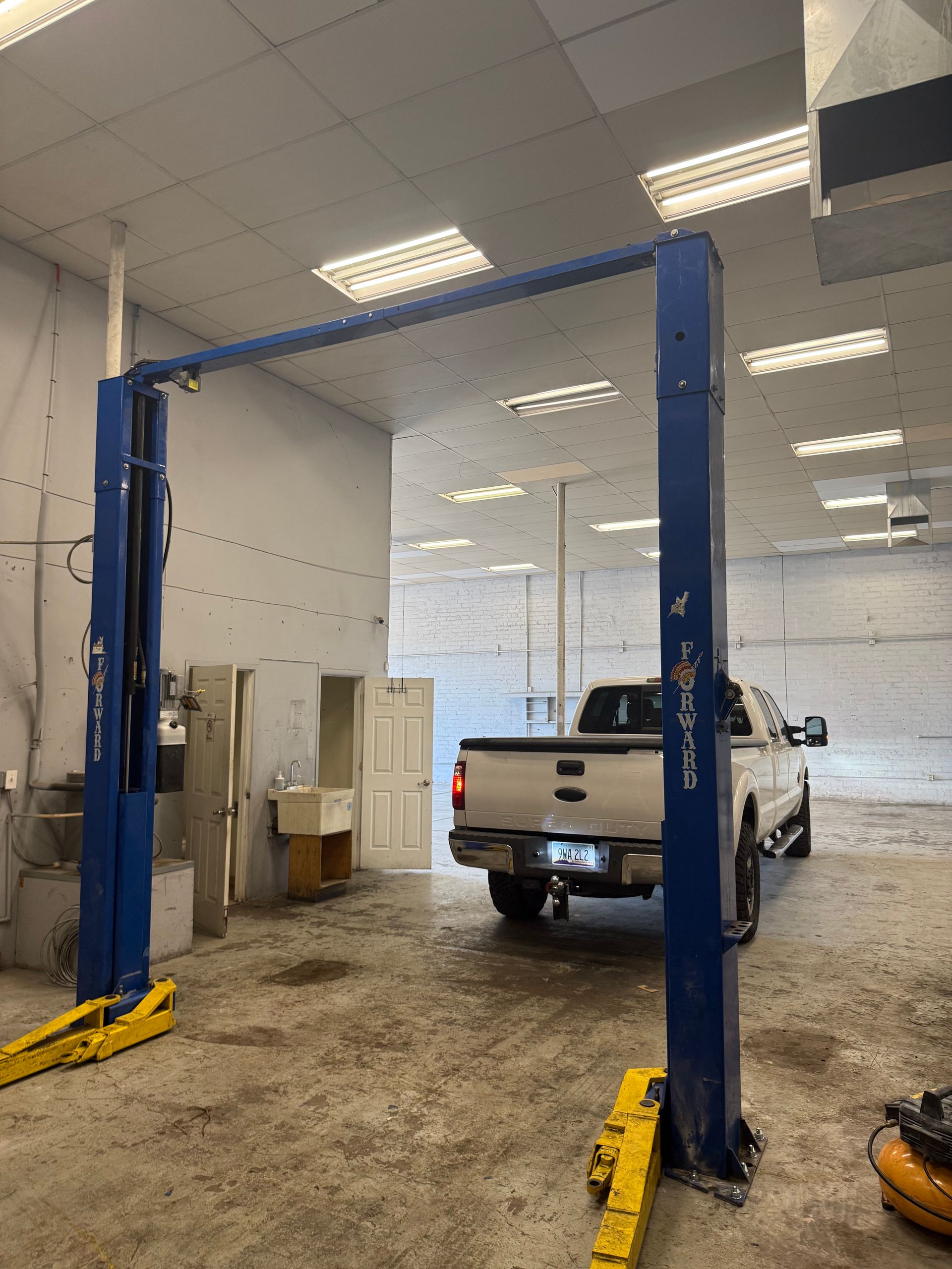 Blue two-post car lift in an auto shop, with a white pickup truck inside the bay.