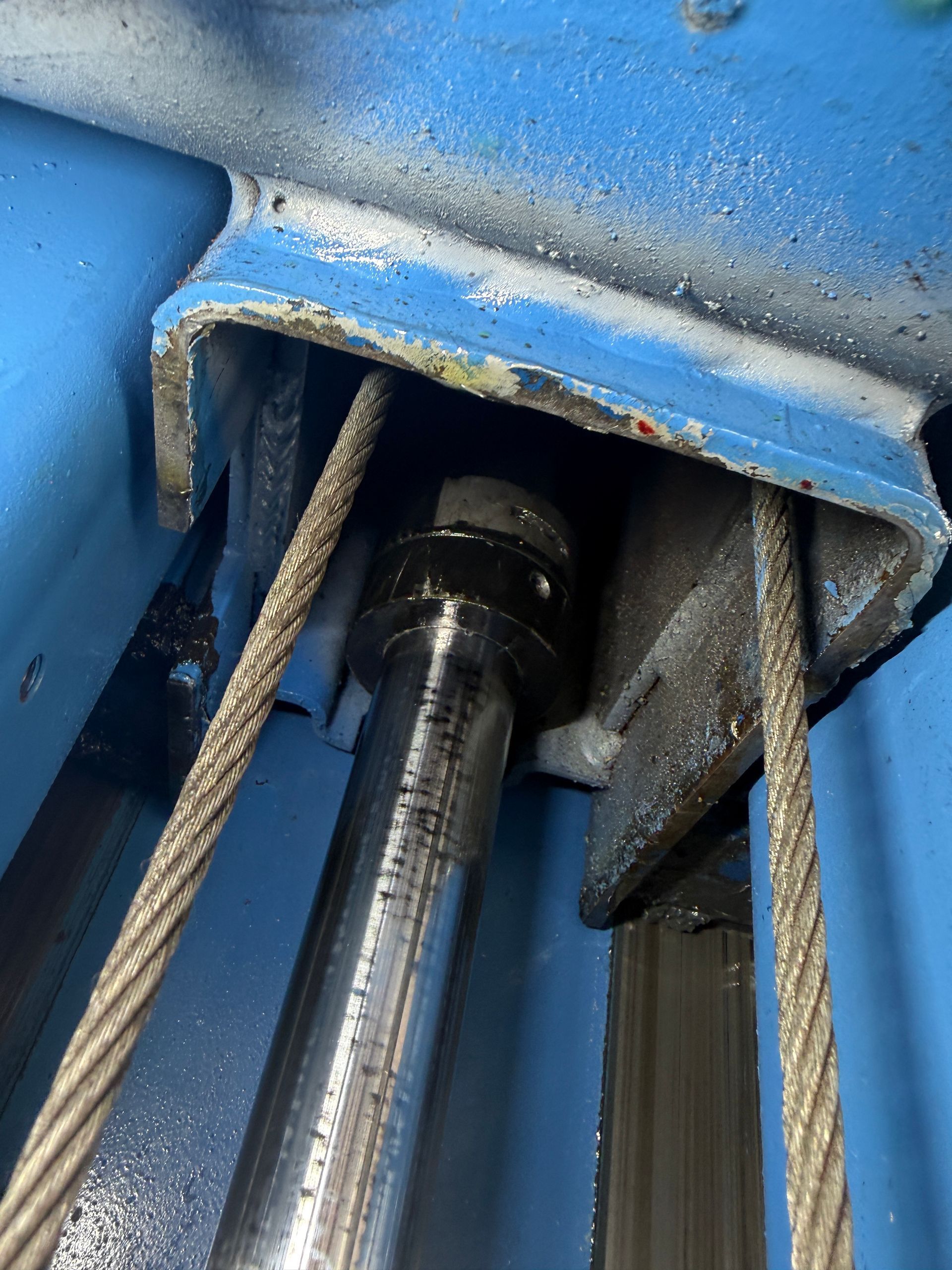 Close-up of a blue metal machine with cables and a black cylinder inside a narrow opening