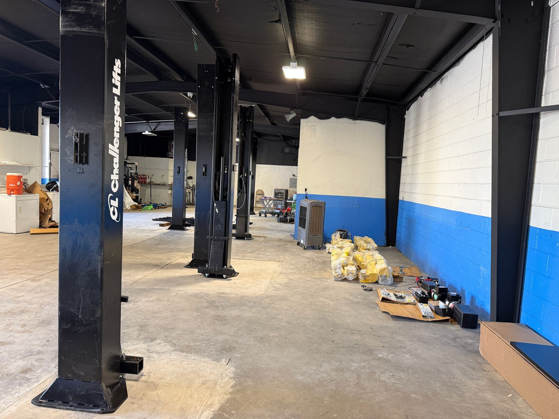 Auto repair shop with blue lift posts, yellow ladder, and equipment on a concrete floor