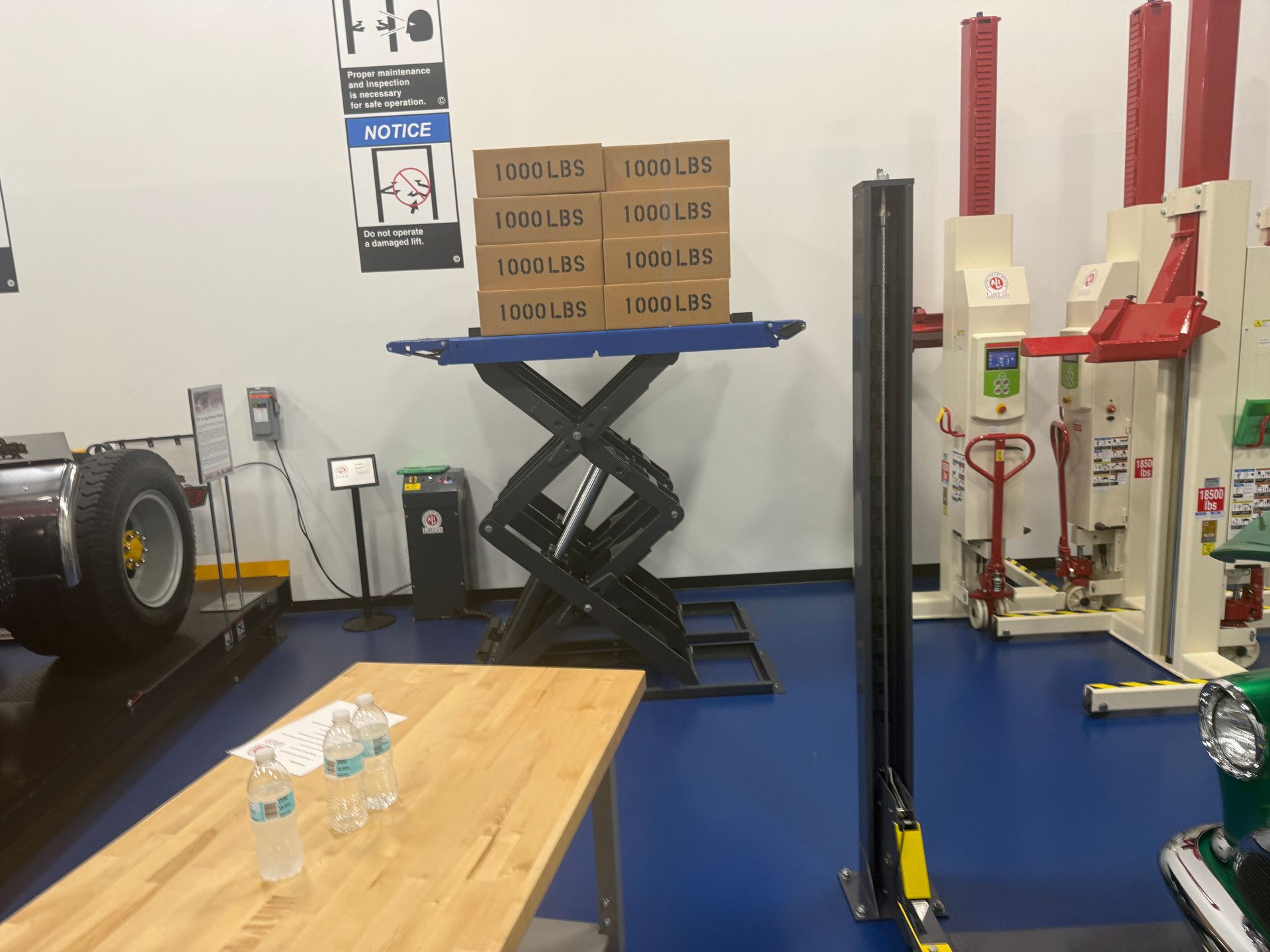 Indoor gym or workshop with equipment, blue chairs along the wall, and black posts on a worn floor.