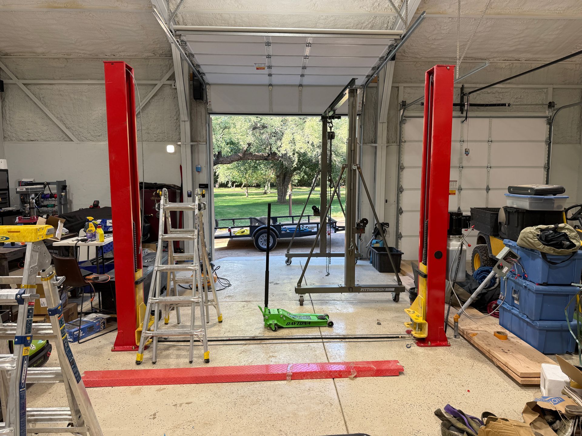 Yellow CAT forklift secured on a blue dual-axle trailer inside a white garage.