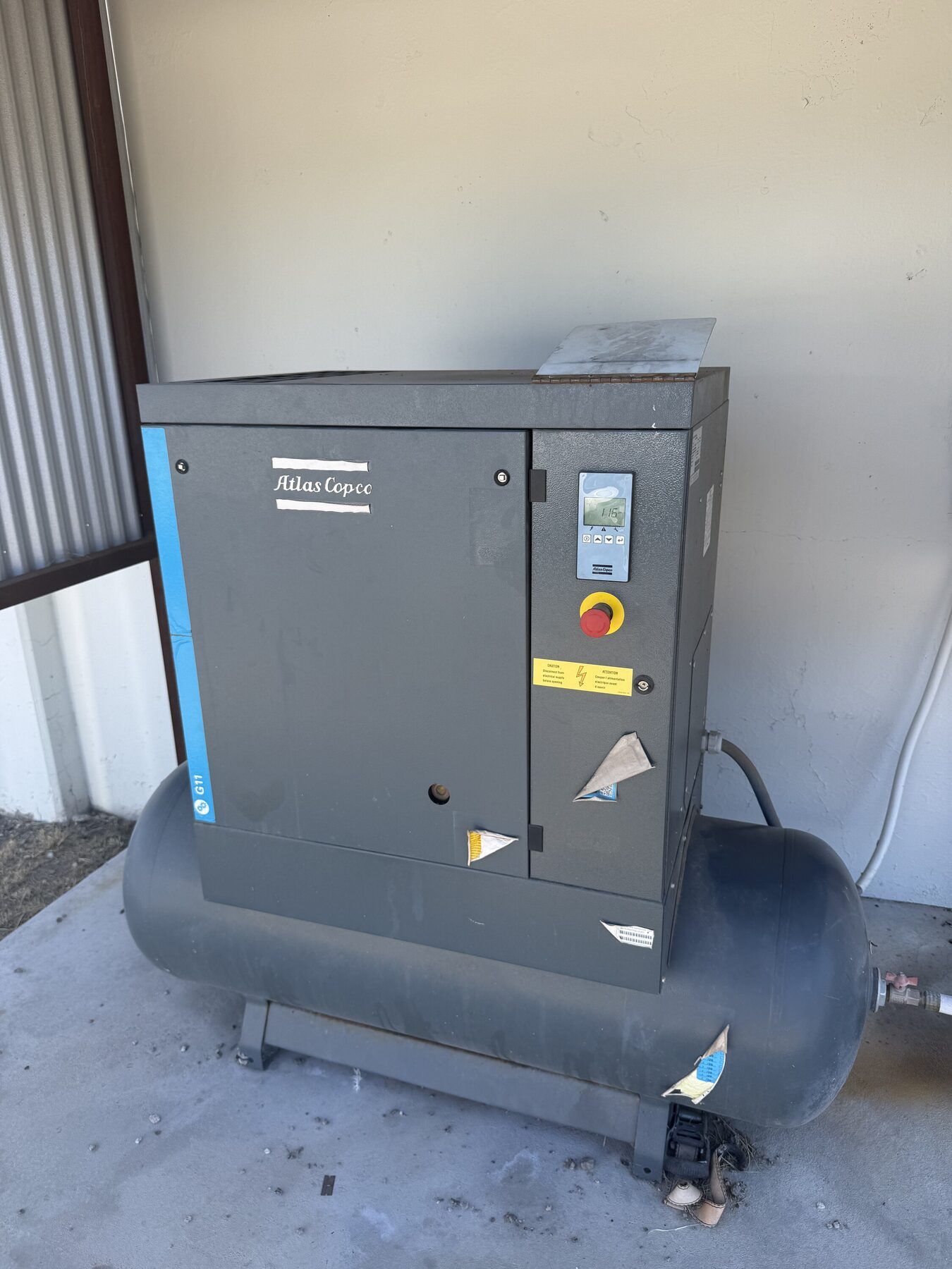 Gray industrial air compressor unit in an outdoor alcove against a wall