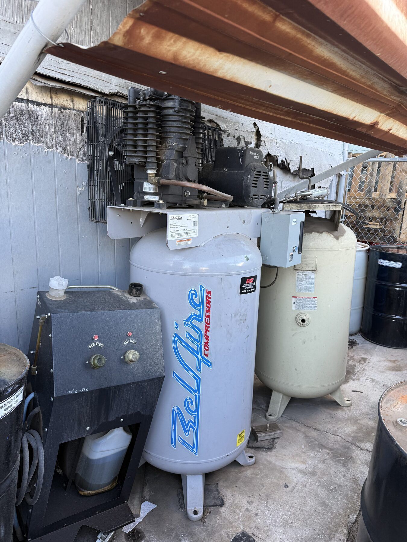 Two large water heaters and utility equipment under a slanted roof in a cramped outdoor space