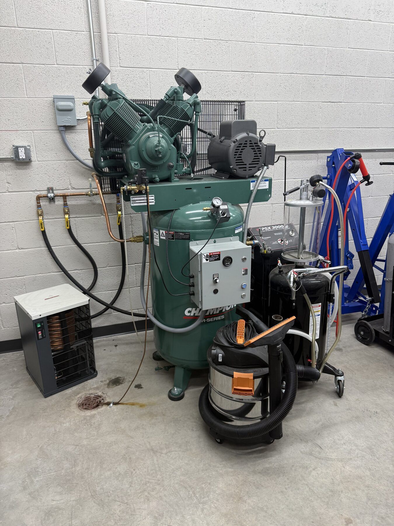 Green industrial air compressor with hoses and tools in a workshop corner