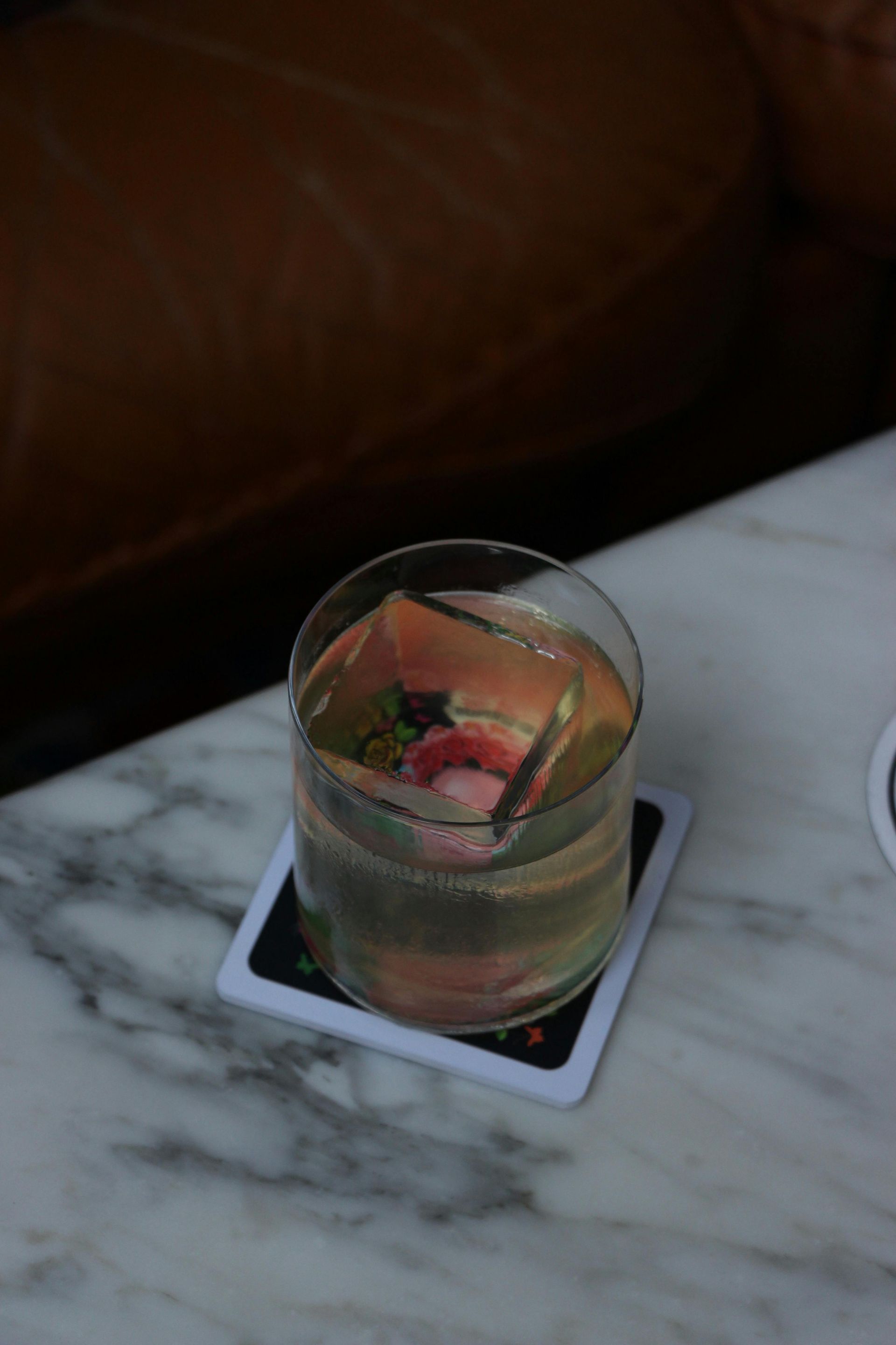 Cocktail servi dans un verre avec des glaçons et une garniture sur un sous-verre, table en marbre, fond en cuir.