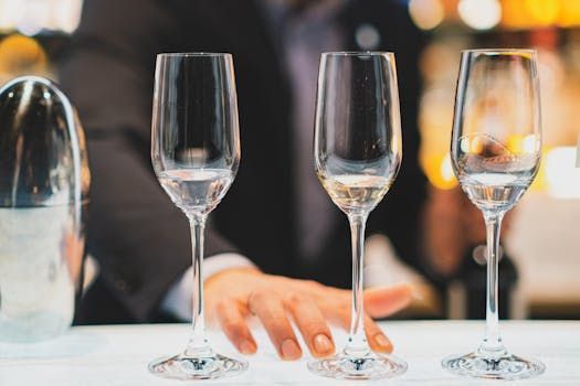 Trois flûtes à champagne vides sur un comptoir blanc, un barman en arrière-plan.
