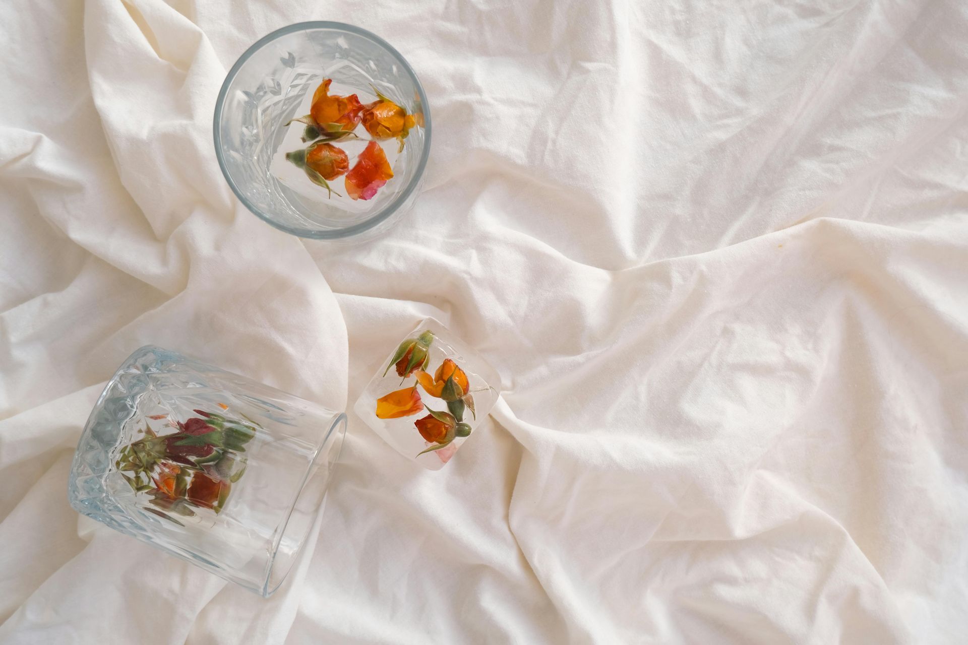 Deux verres avec des glaçons à motifs floraux posés sur un tissu blanc froissé.