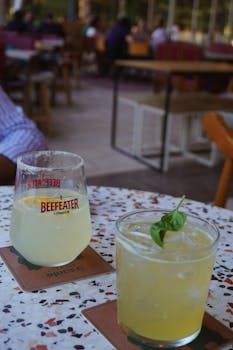 Deux cocktails sur une table mouchetée, dans un bar en plein air. L'un d'eux est agrémenté d'une tranche de citron.