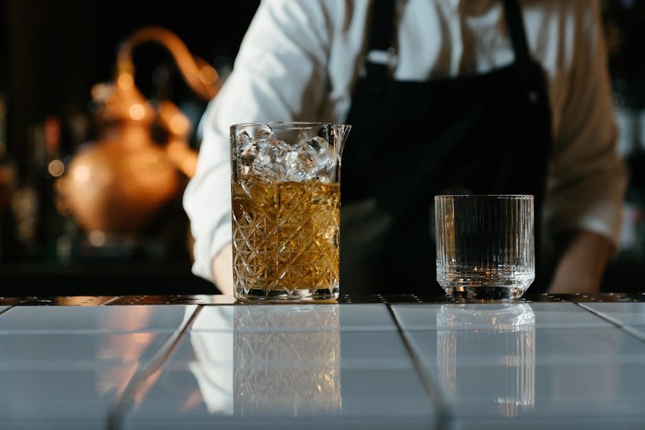 Barman avec un verre à mélange rempli de glace et un verre sur le comptoir. Alambic en cuivre en arrière-plan.