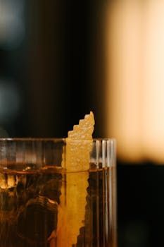 Cocktail servi dans un verre, garni d'un zeste de citron, gros plan sur fond flou.
