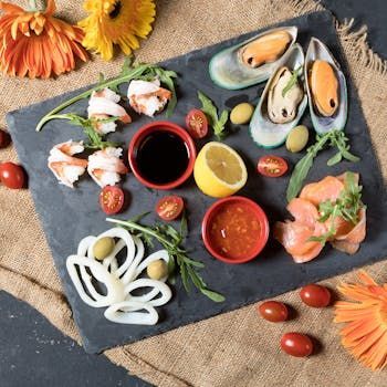Assiette de fruits de mer en apéritif avec crevettes, moules, calamars, saumon, sauces, citron et tomates.