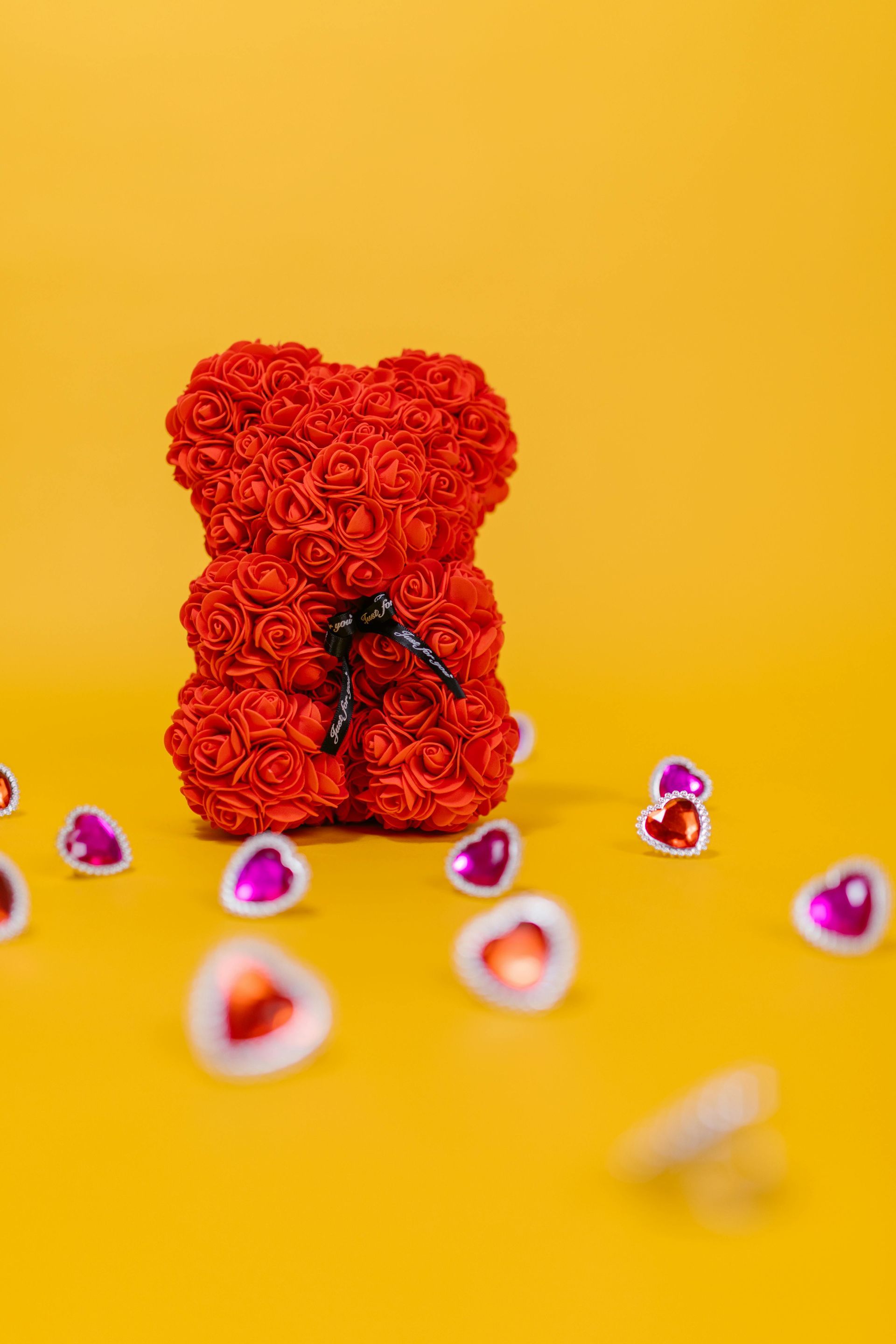 Ours en forme de rose rouge avec un nœud noir, entouré d'autocollants en forme de cœur sur fond jaune.