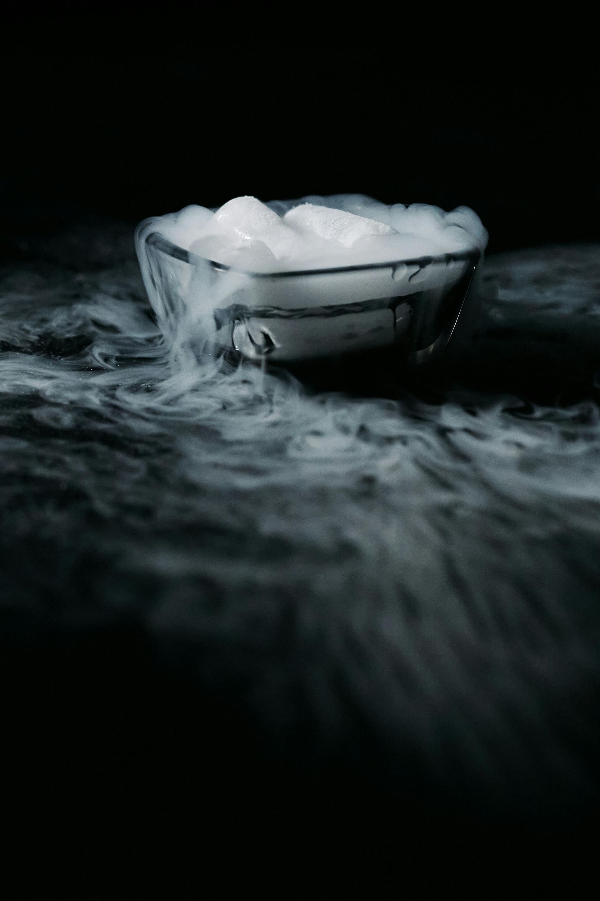 Bol de glace blanche, d'où s'échappe du brouillard sur fond noir.