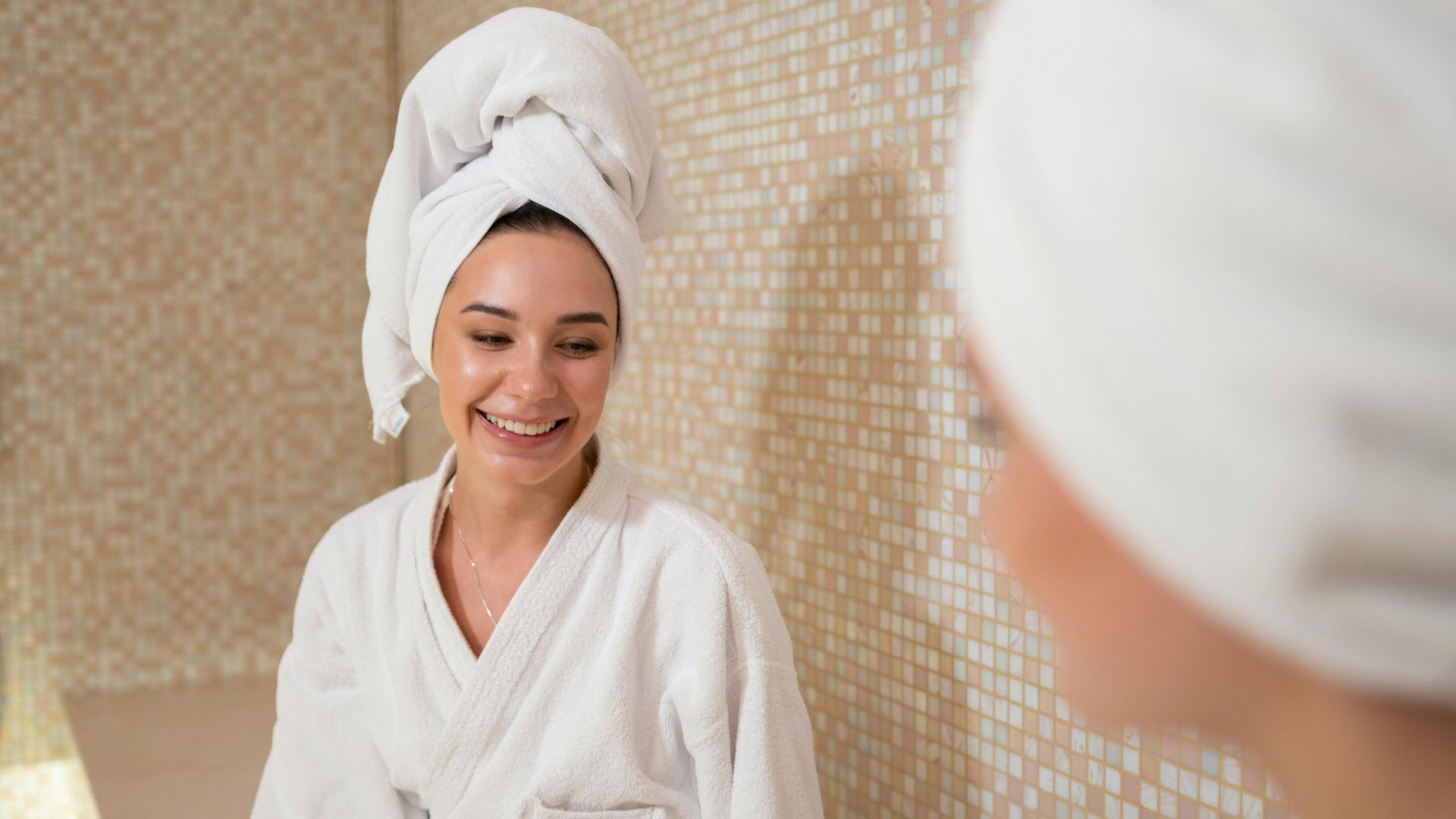 Woman in a white robe and towel smiling in a spa room with mosaic tile walls