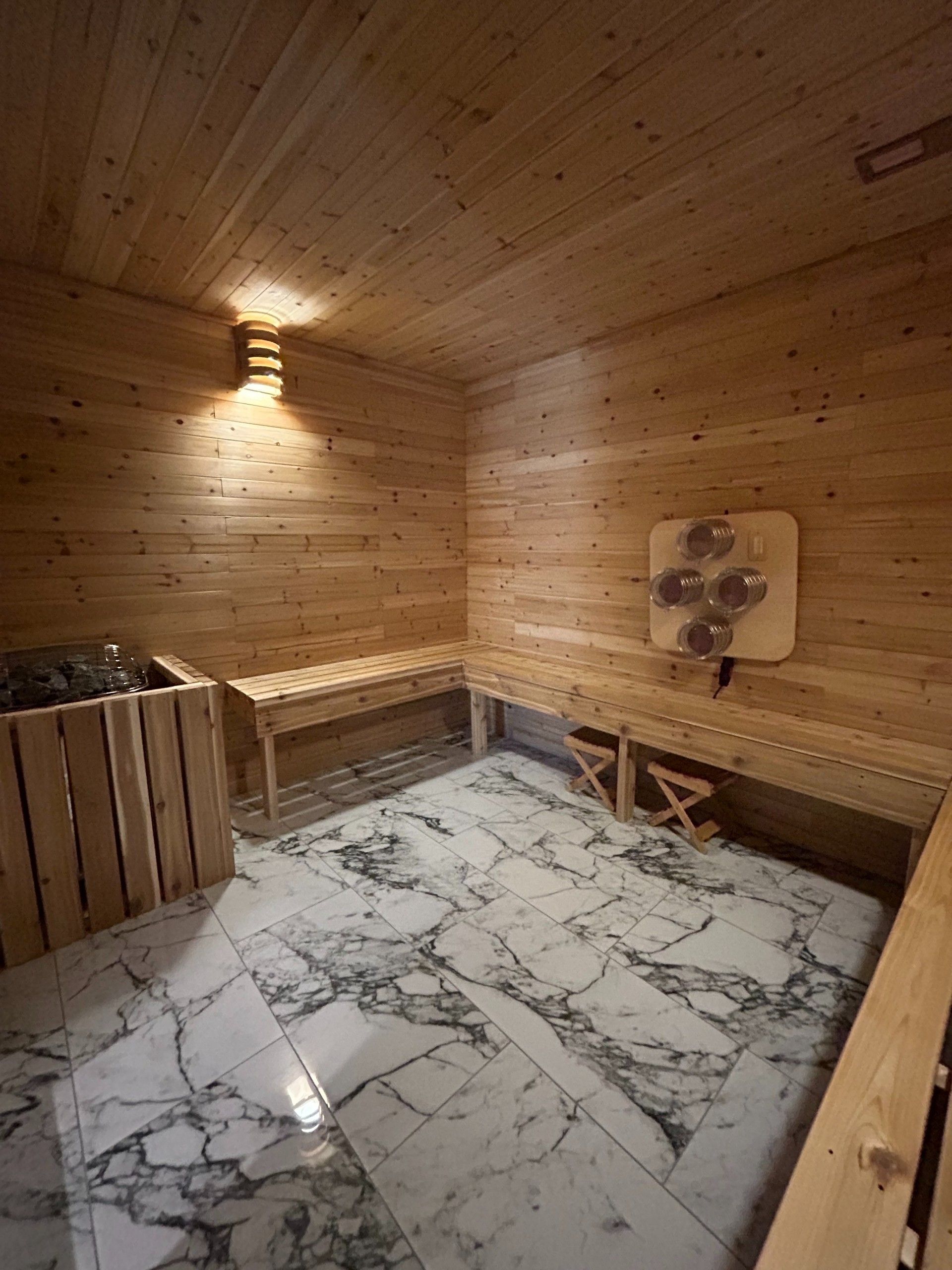 Wood-paneled sauna room with marble-pattern floor, bench seating, and warm wall light