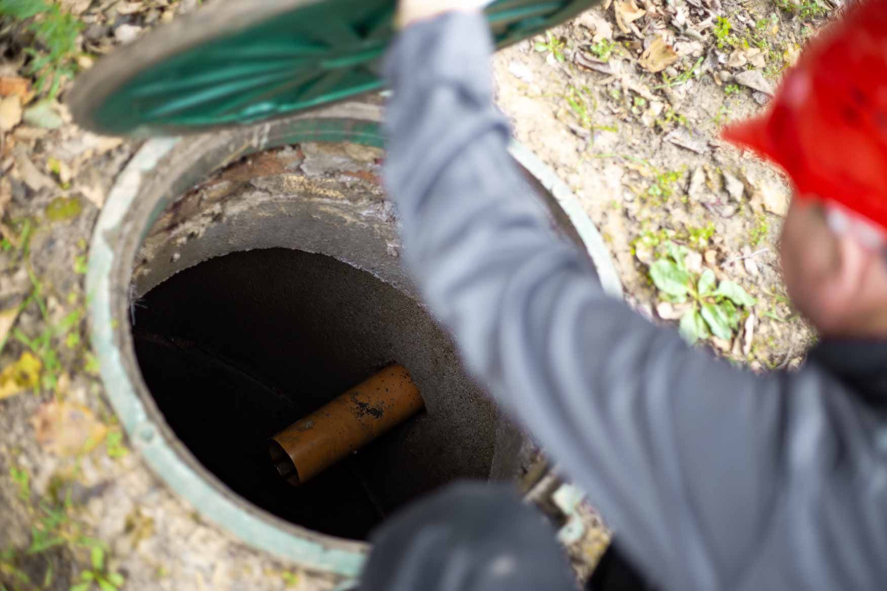 Worker peering into open manhole with a wooden pipe inside
