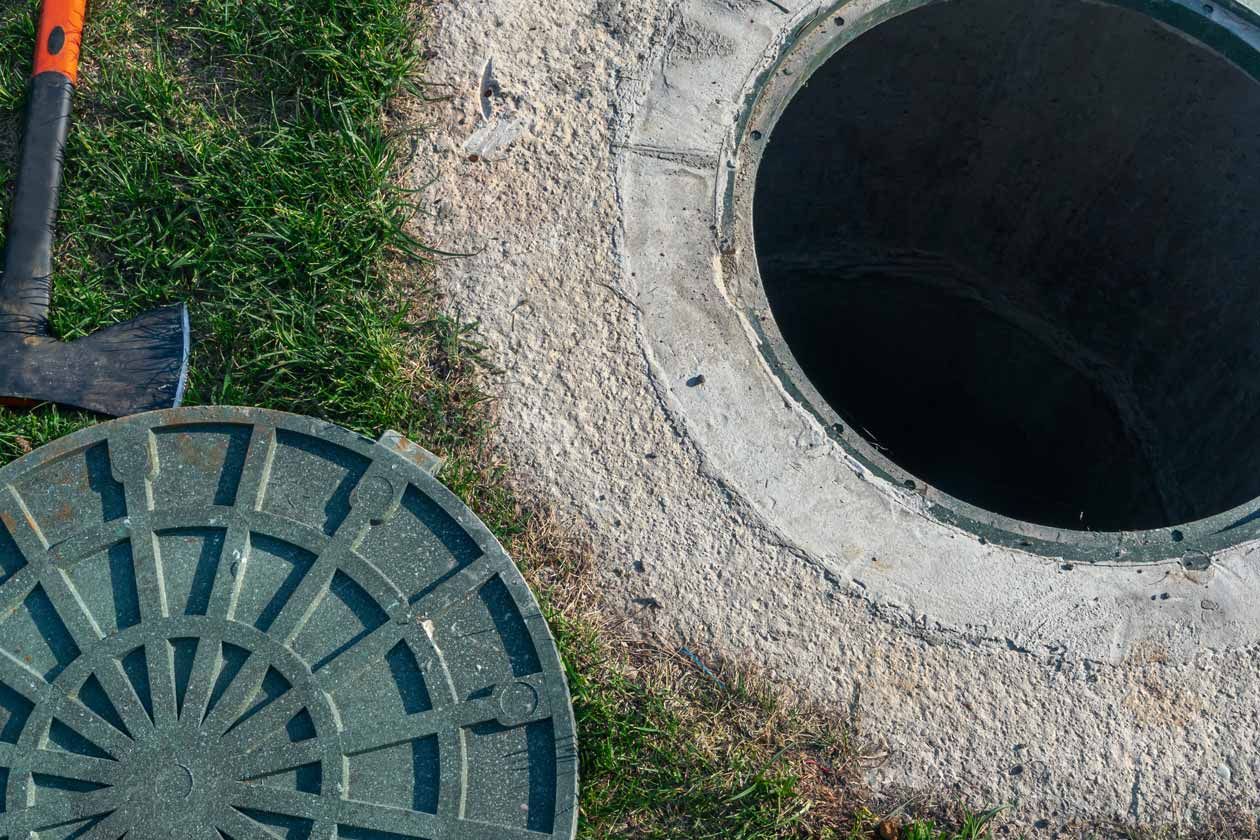 Open manhole and circular sewer cover on gravel beside grass