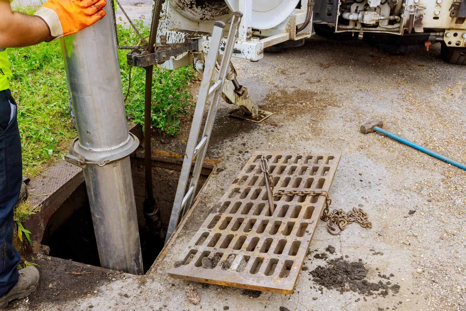Worker in orange gloves handling a concrete pipe near an open drain grate on a wet roadside