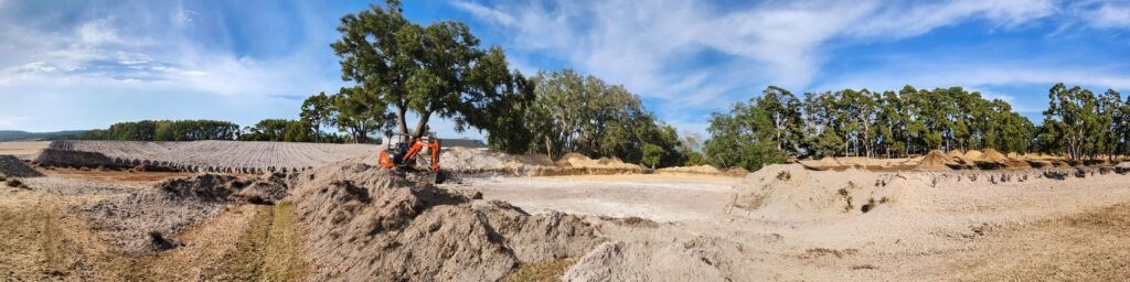 Person on an orange dirt bike riding across a sandy trail with trees and blue sky in the background