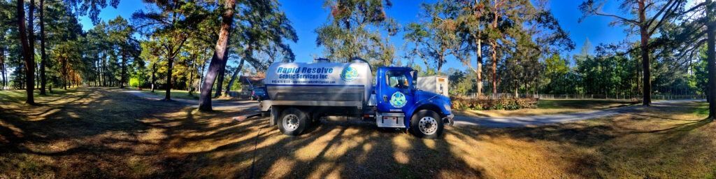 Blue truck parked on a dirt road in a wooded area under a bright blue sky