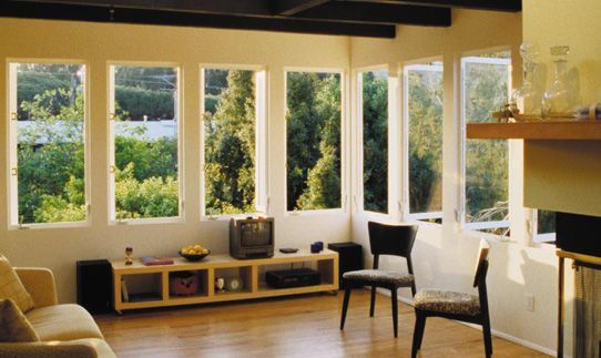 Living room with large windows overlooking trees, featuring wooden floors, a couch, and entertainment center.