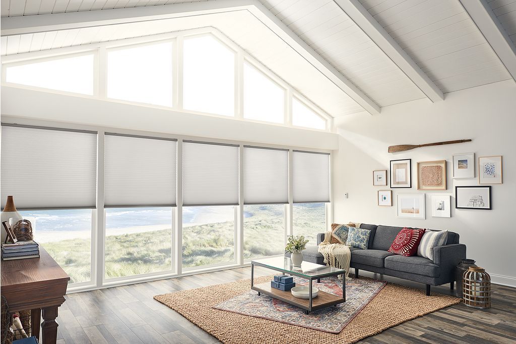 Living room with large windows, white walls, angled ceiling, sofa, rug, and artwork.