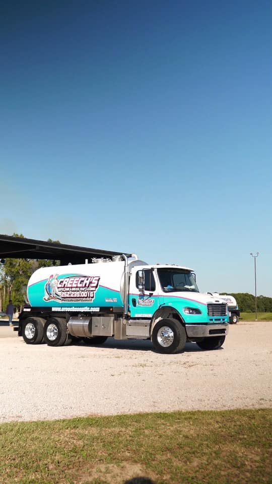 A white and turquoise septic tank truck parked outdoors under a blue sky.