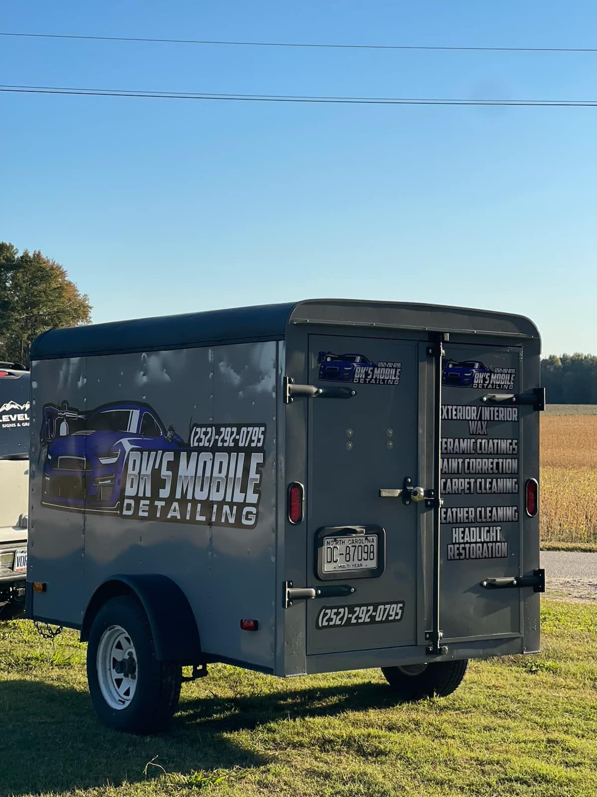 Gray mobile detailing trailer in a grassy field on a sunny day.
