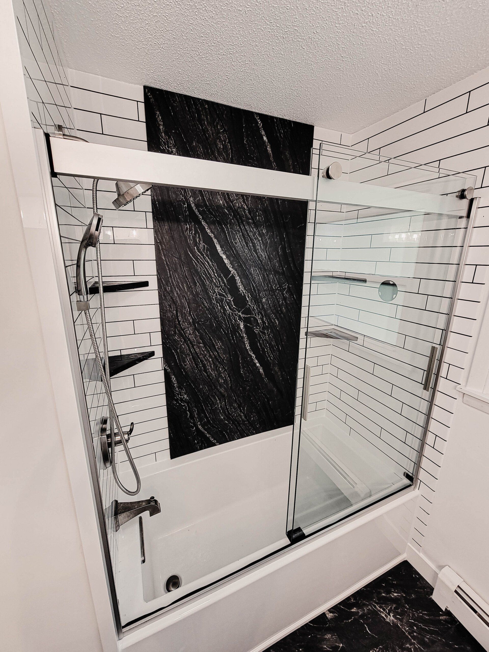 Modern shower with glass enclosure, chrome fixtures, white tile, and black accent panels