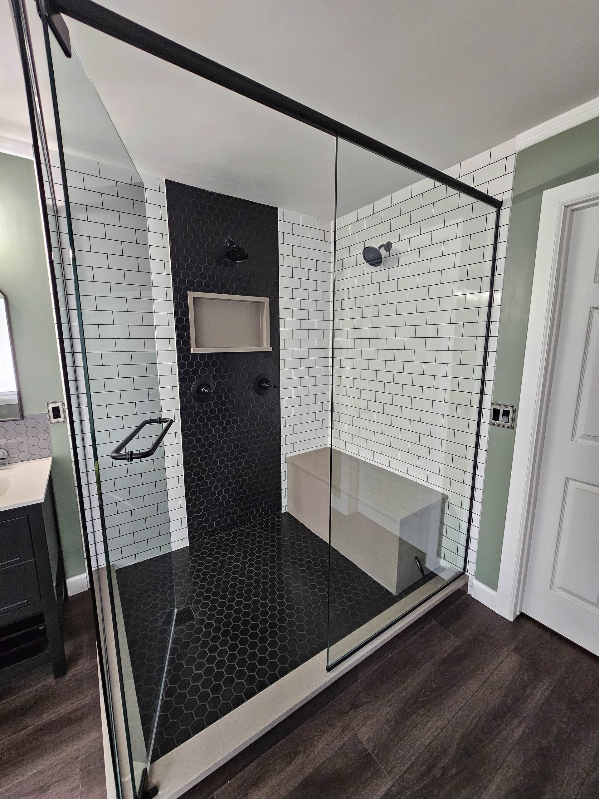 Modern walk-in shower with black tile accent wall, glass enclosure, white subway tiles, and bench