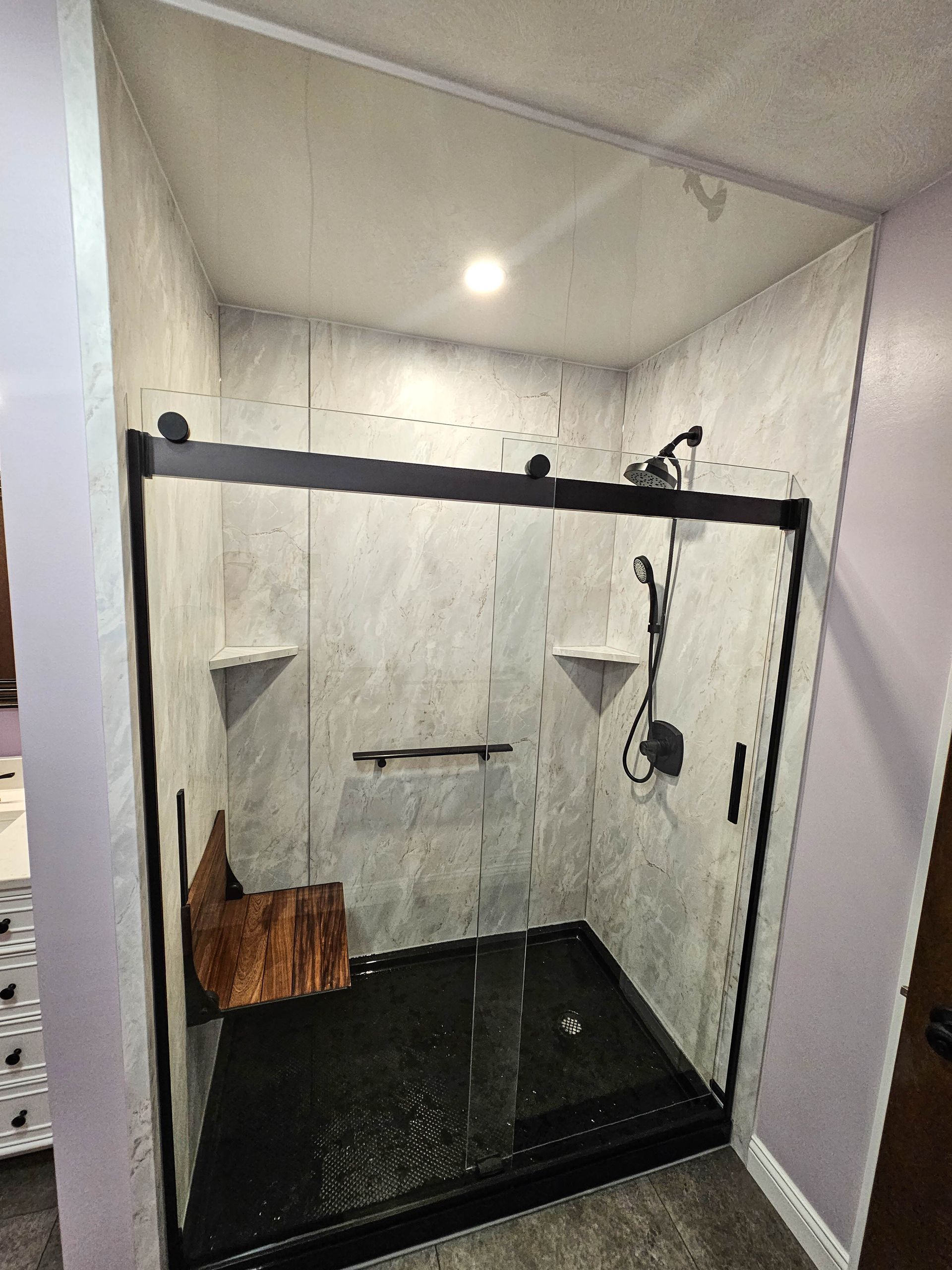 Glass-enclosed tiled shower with black trim, built-in shelves, and a bench seat