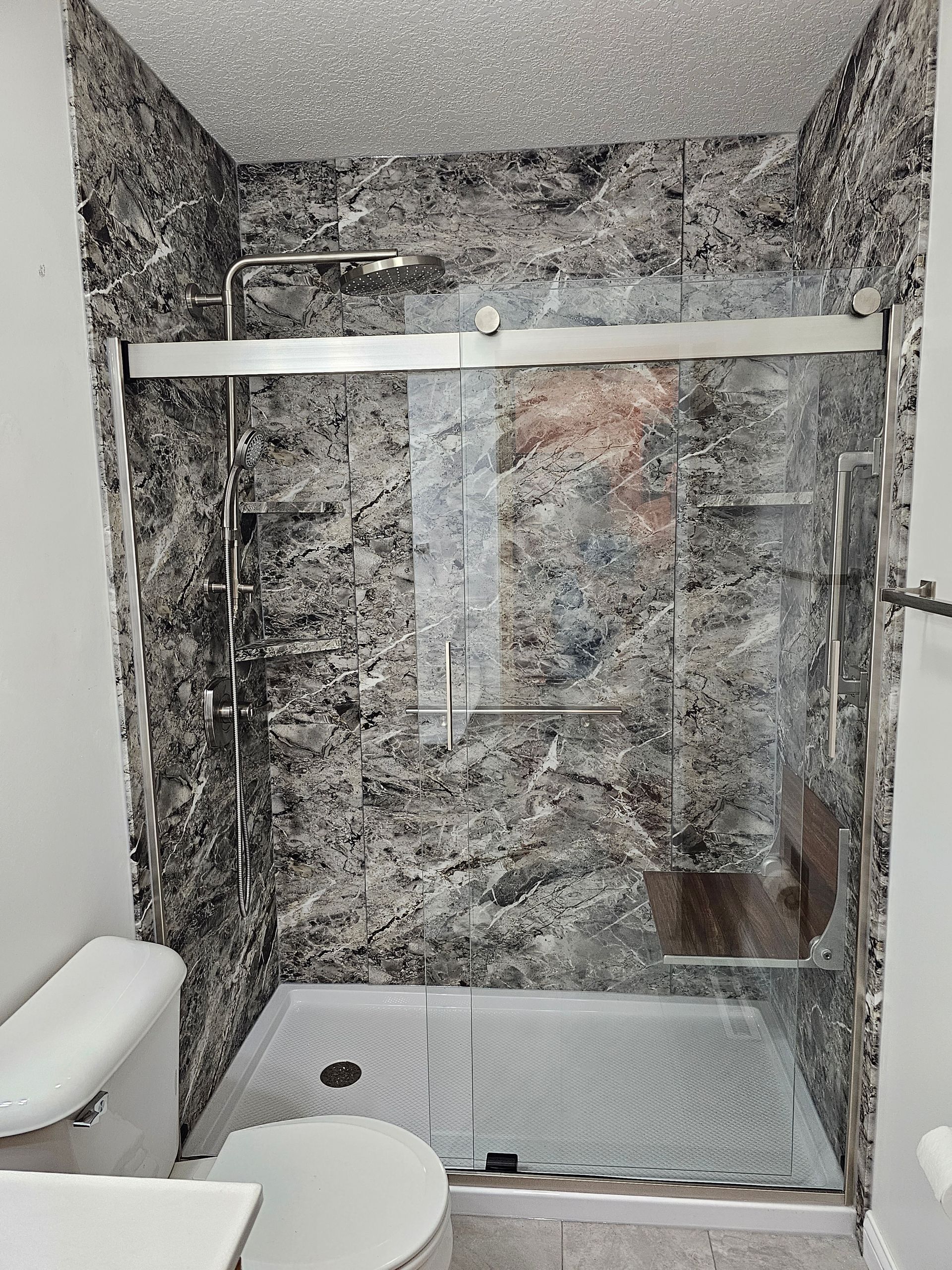 Modern bathroom with gray marble walls, glass shower enclosure, and toilet beside a shower bench