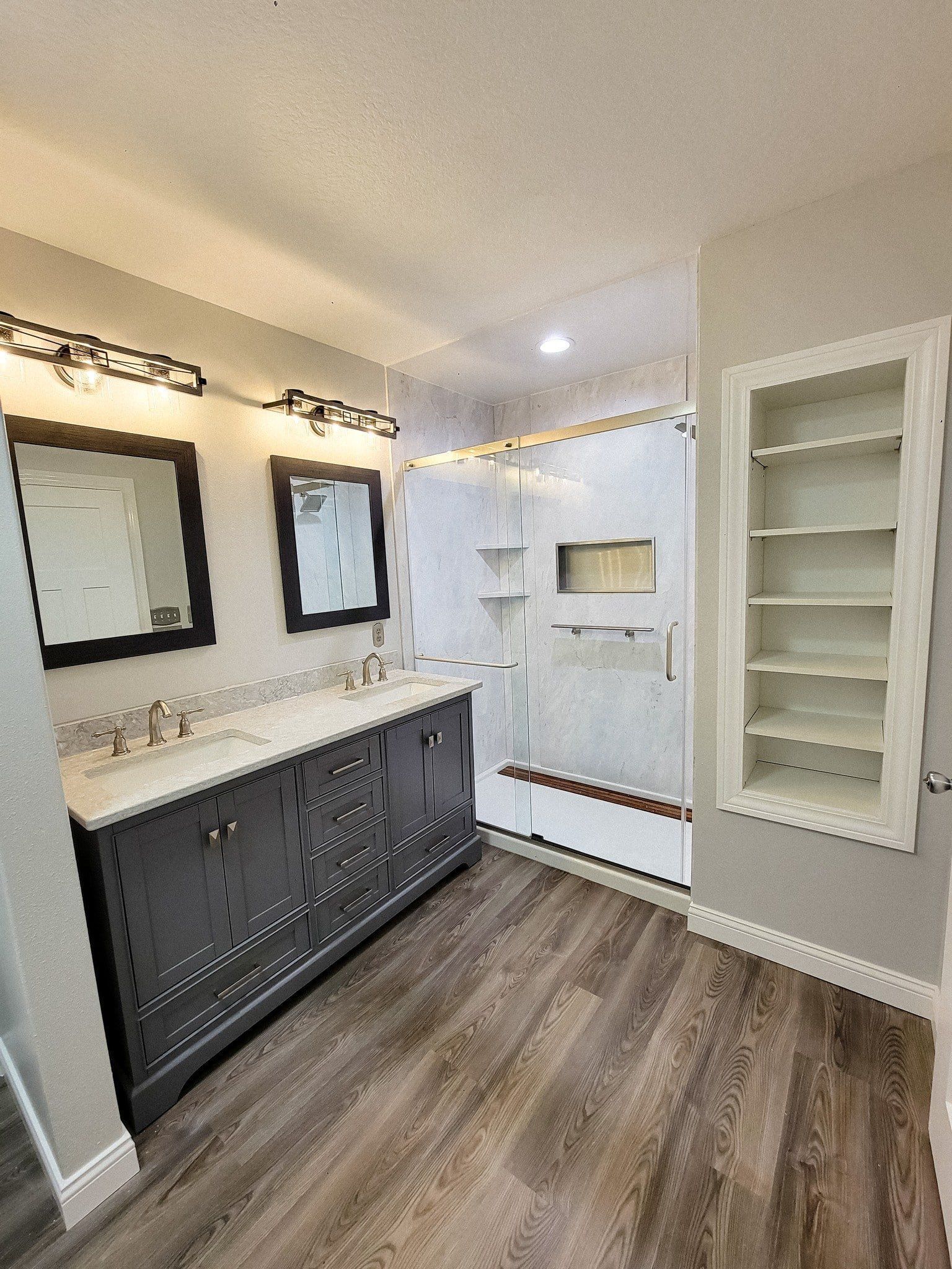 Modern bathroom with dark vanity, white countertop, mirror lights, and built-in shelves.