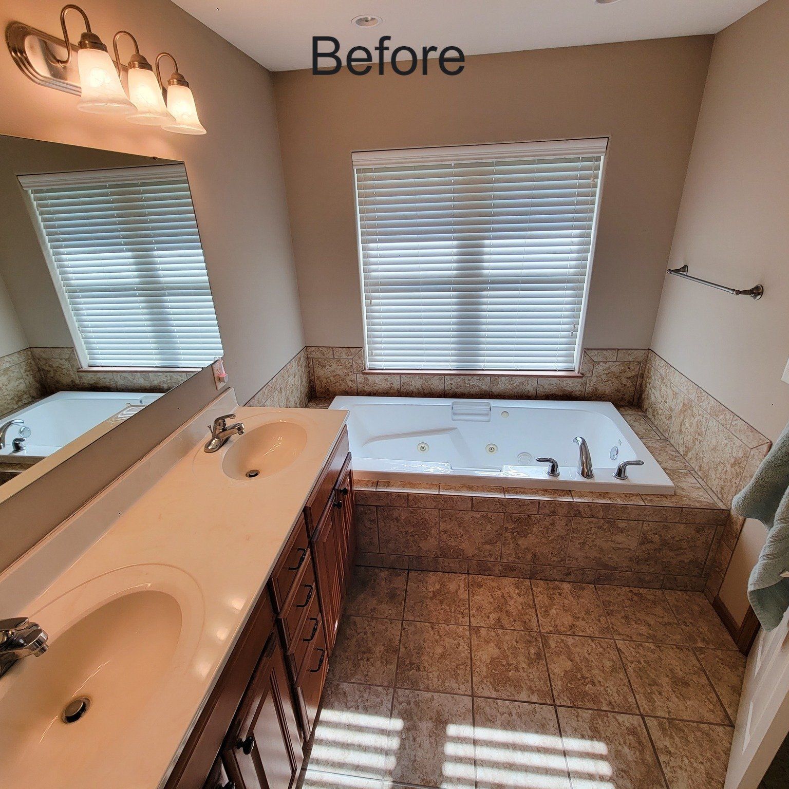 Before view of a beige bathroom with a vanity, bathtub, and two windows with blinds