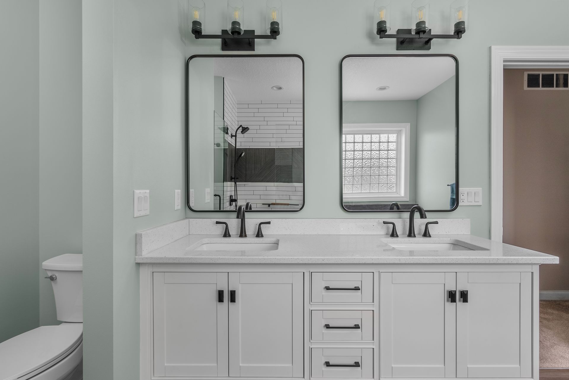 Bright bathroom vanity with double sinks, mirrors, and white cabinets on pale walls