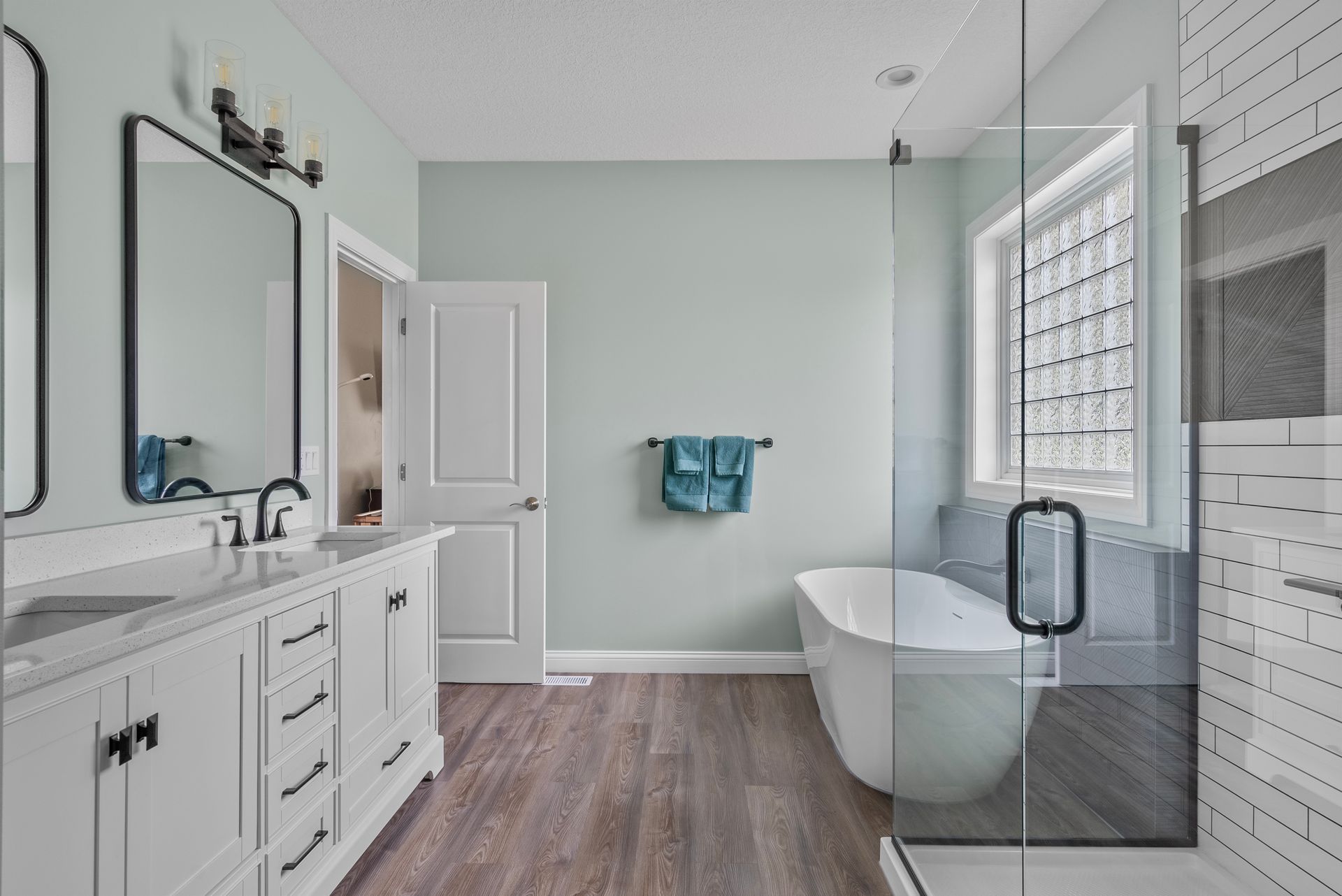 Modern bathroom with vanity, freestanding tub, glass shower, and gray wood-look floor