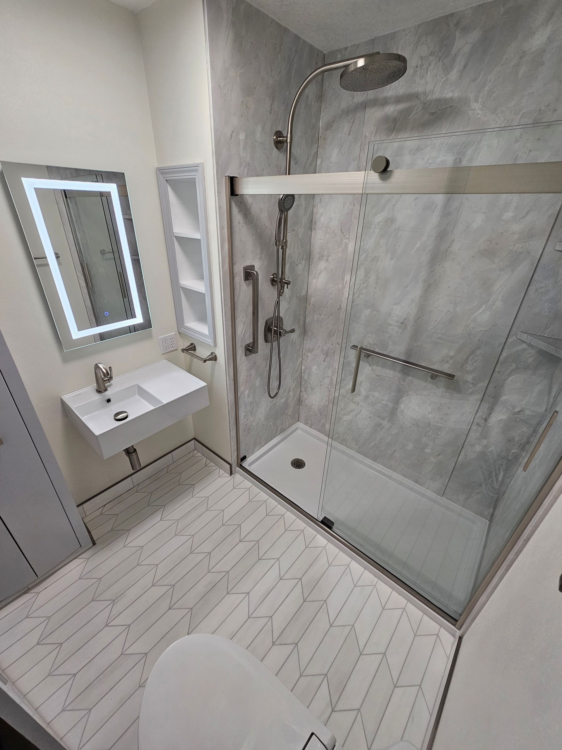Modern accessible bathroom with walk-in shower, wall sink, mirror, and gray tile floors and walls