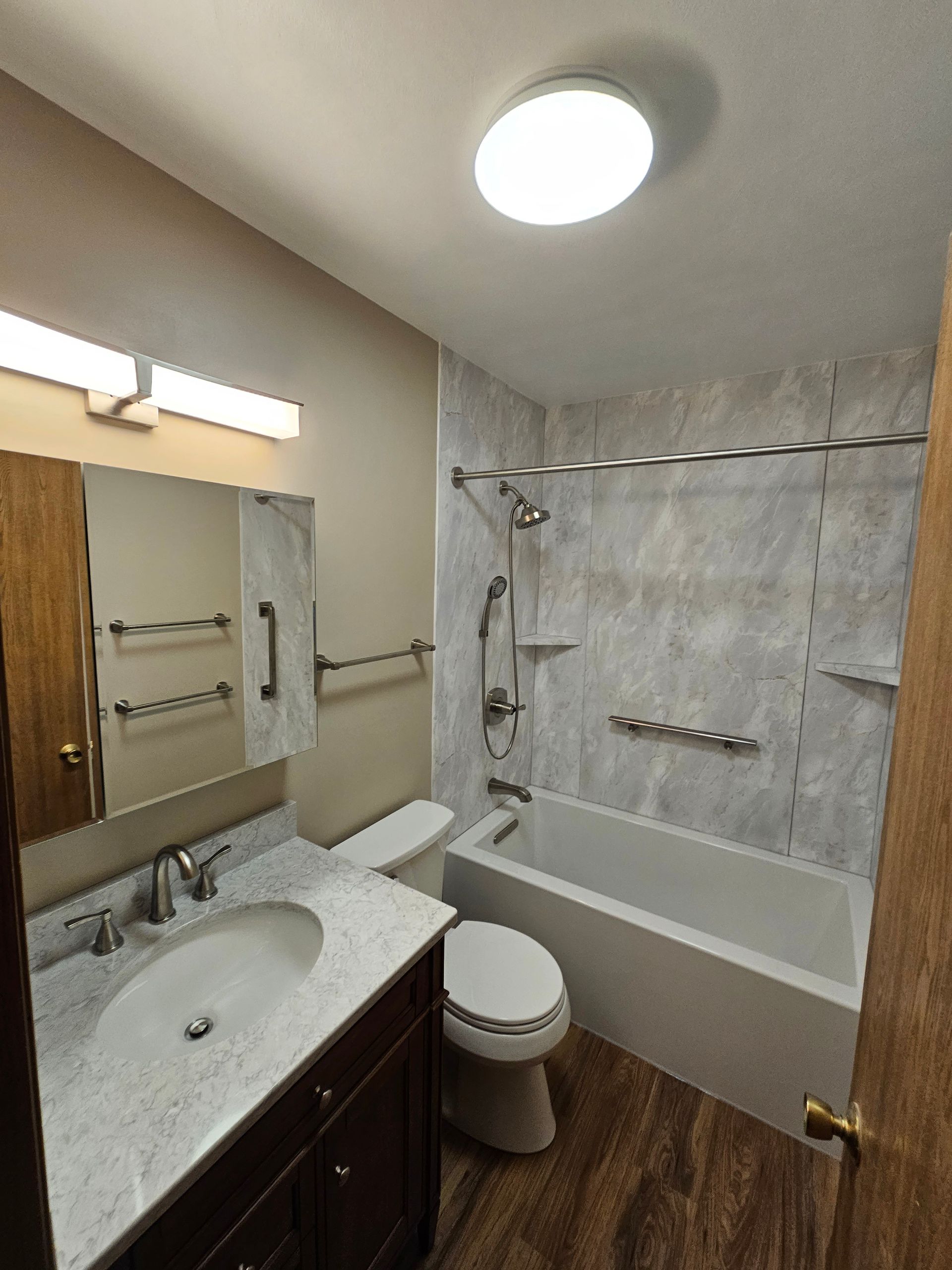 Small bathroom with sink, toilet, bathtub, and wood-look floor, lit by a ceiling light.