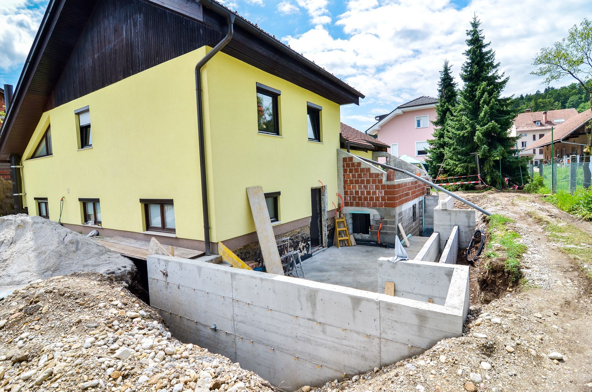 Yellow House With New Concrete Foundation Construction Next to It — Scott Graham Building Services In Mermaid Beach, QLD